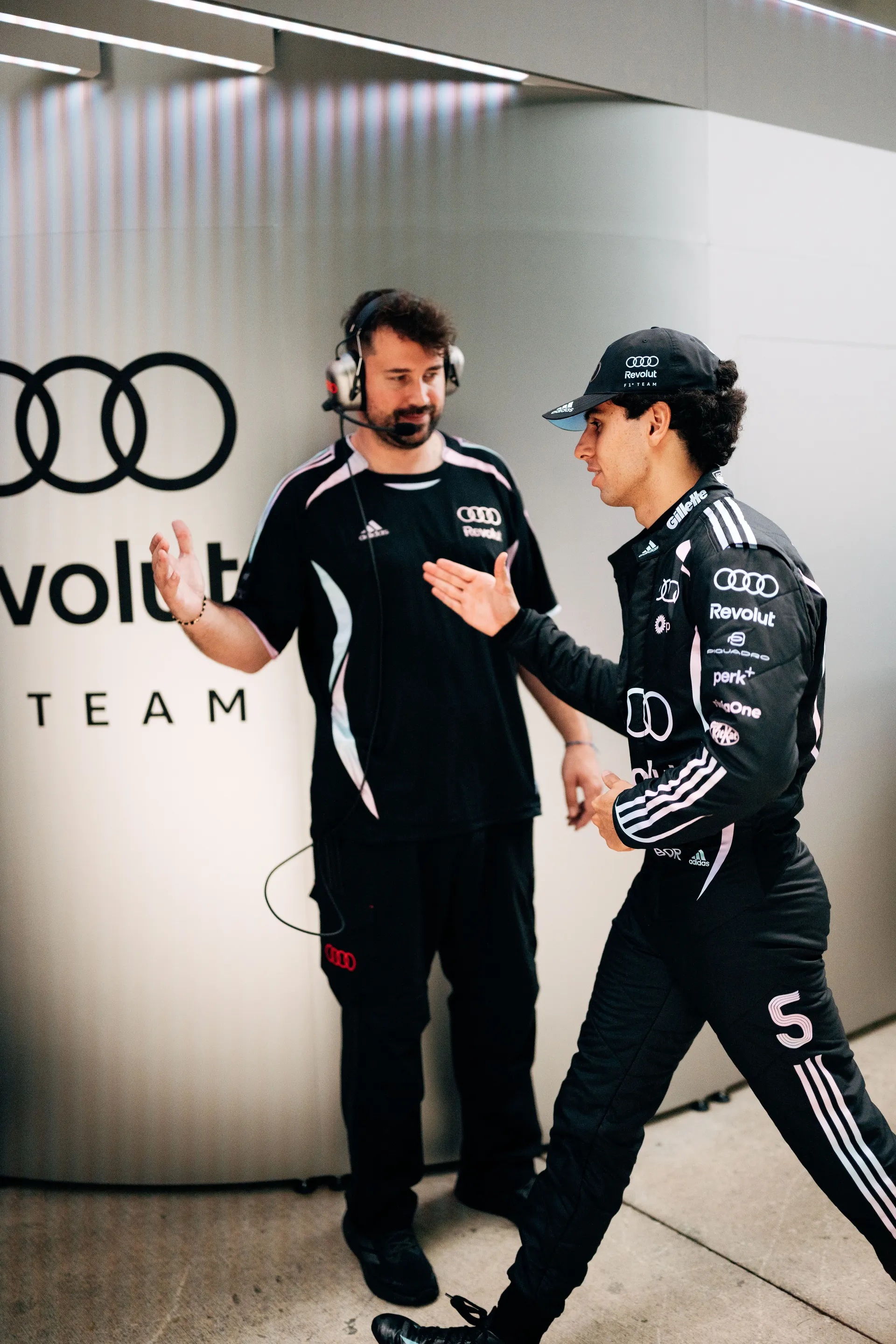 Gabriel Bortoleto in Audi Revolut F1® Team race suit discussing with an engineer inside the garage, gesturing during a pre-session briefing.