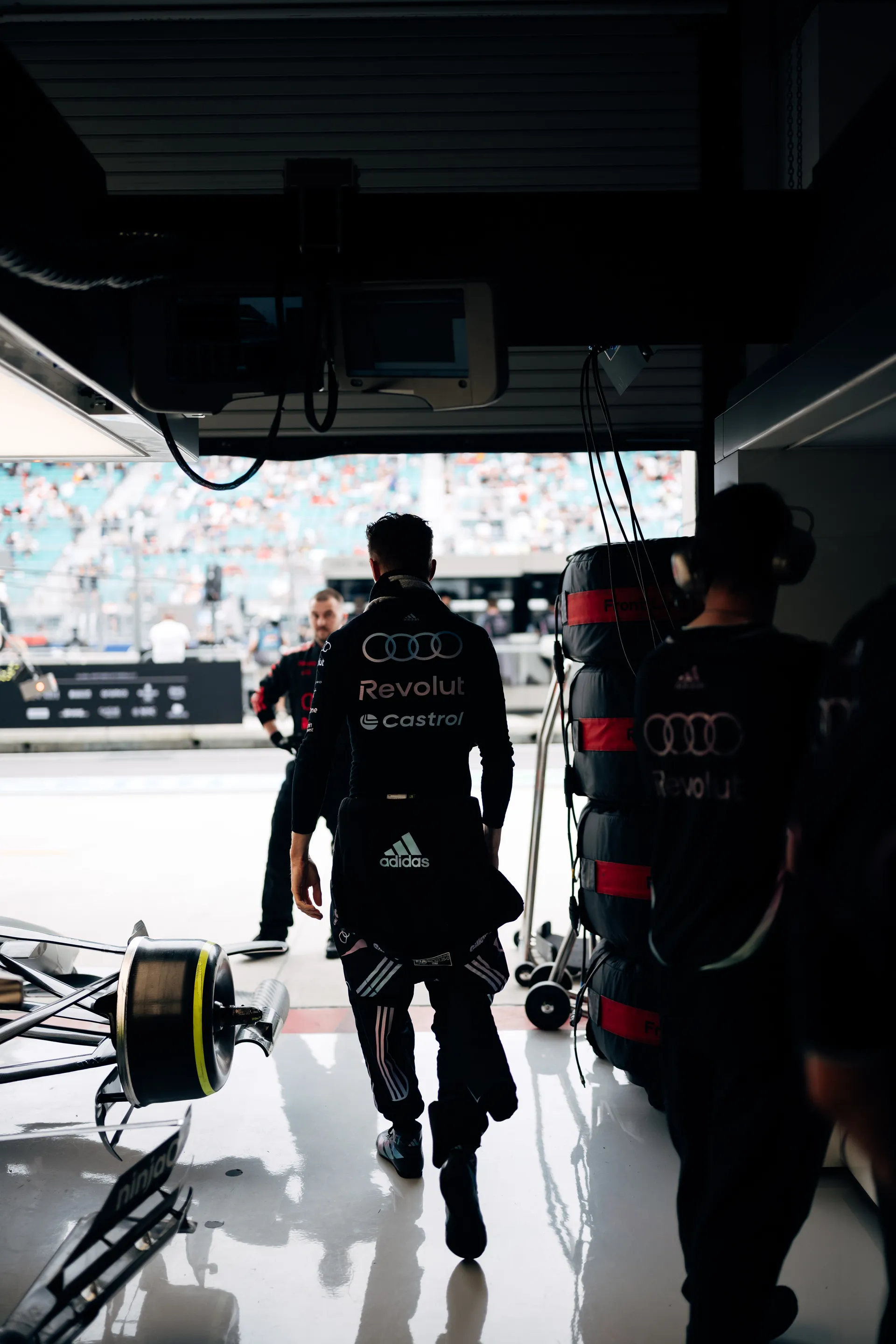 Nico Hulkenberg entering the Audi Revolut F1® Team garage from the pit lane, seen from behind with equipment and tires stacked nearby.