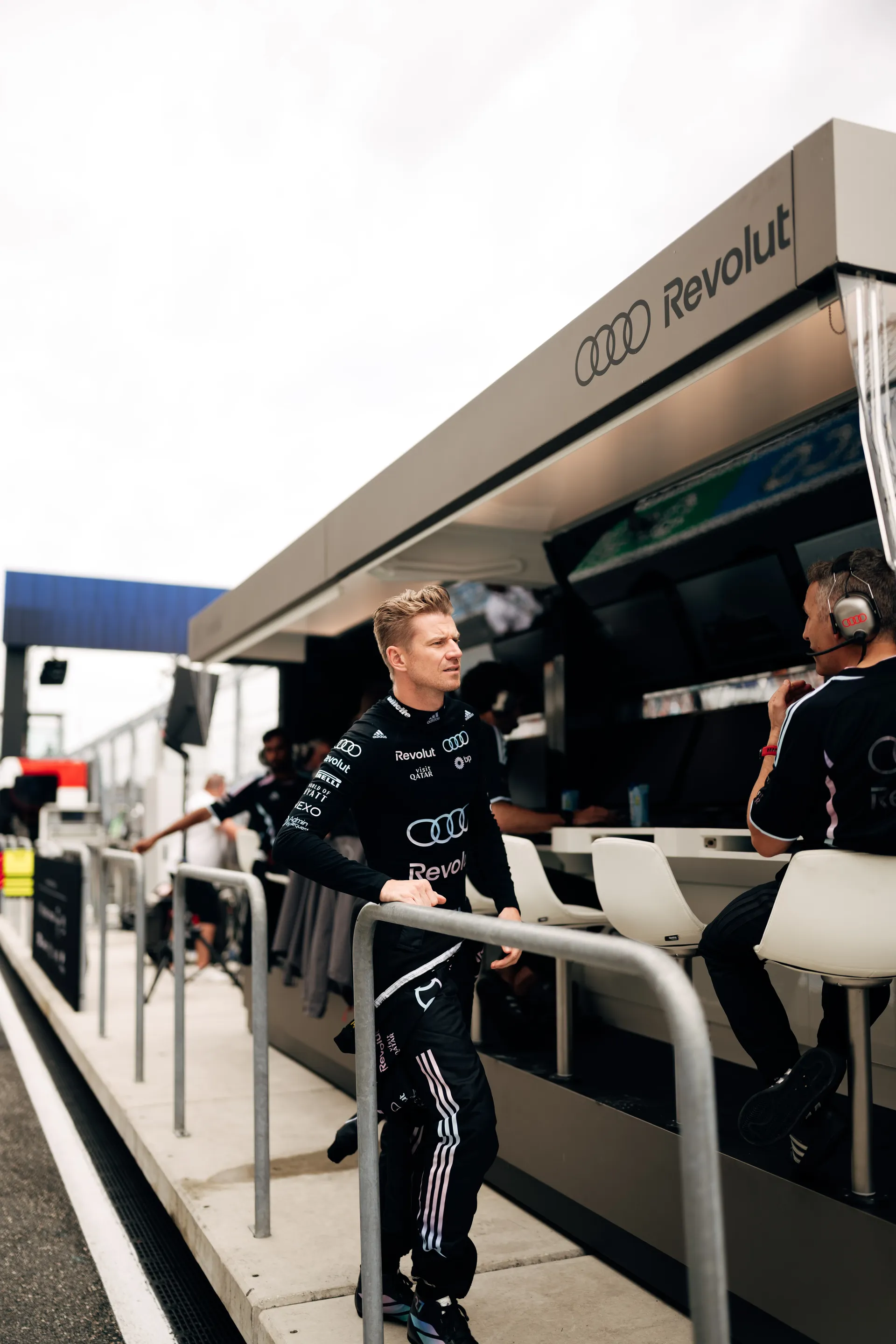 Nico Hulkenberg standing trackside at the Audi Revolut F1® Team pit wall, looking toward the circuit while speaking with a team member.