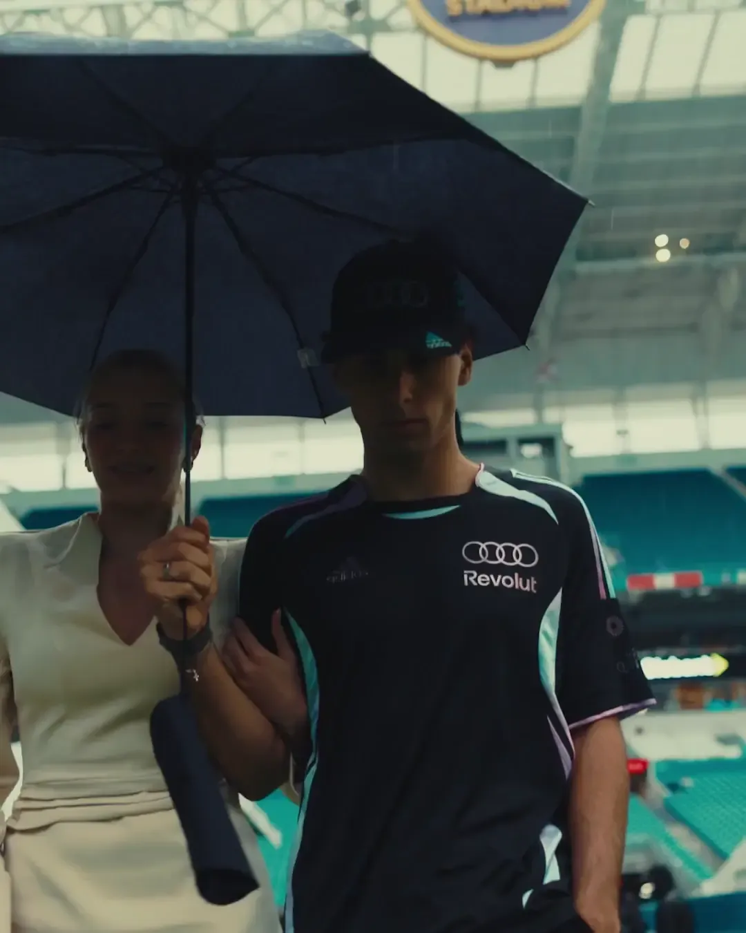 Gabriel Bortoleto arrives with a guest under an umbrella at the Miami International Autodrome ahead of the 2026 Miami Grand Prix sessions.