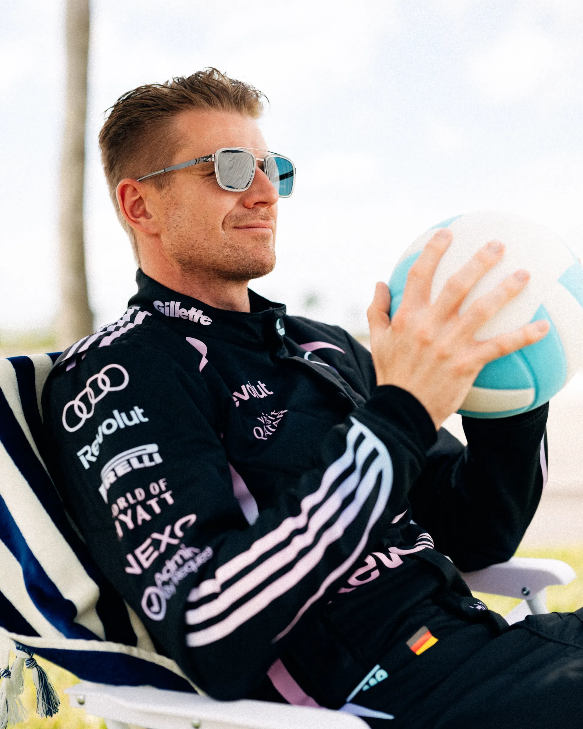 Nico Hulkenberg sits in a striped beach chair holding a blue and white beach ball, wearing sunglasses and the Audi Revolut F1® Team Miami race suit.