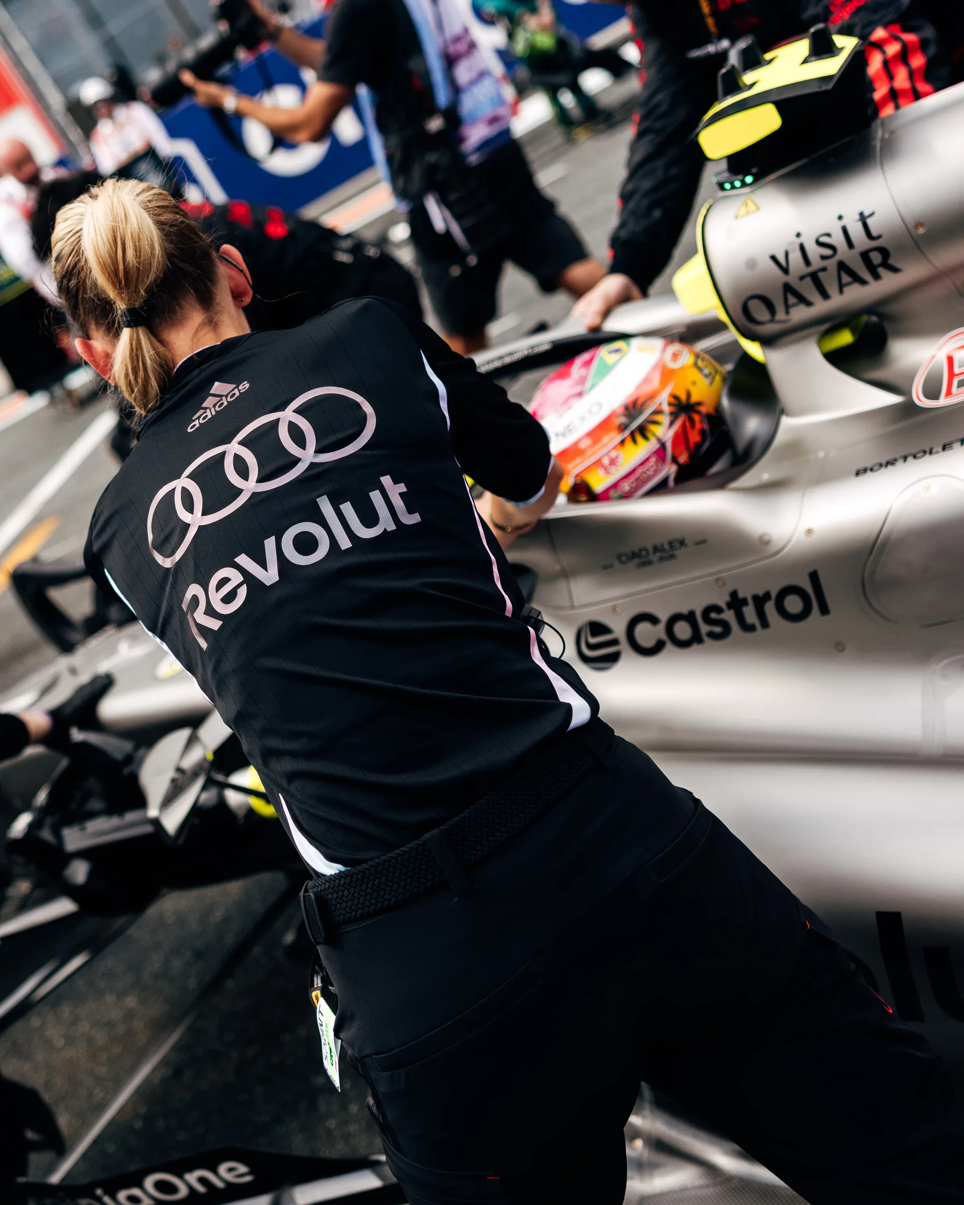 Female Audi Revolut F1® Team crew member leans over Gabriel Bortoleto’s car on the grid, with his colorful helmet visible in the cockpit.