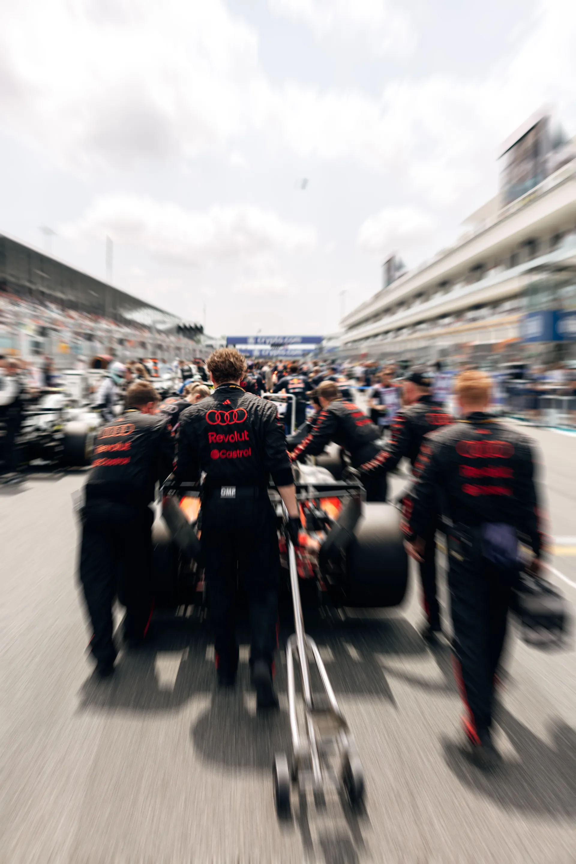 Audi Revolut F1® Team crew push Gabriel Bortoleto’s car down the grid, captured with motion blur from behind.