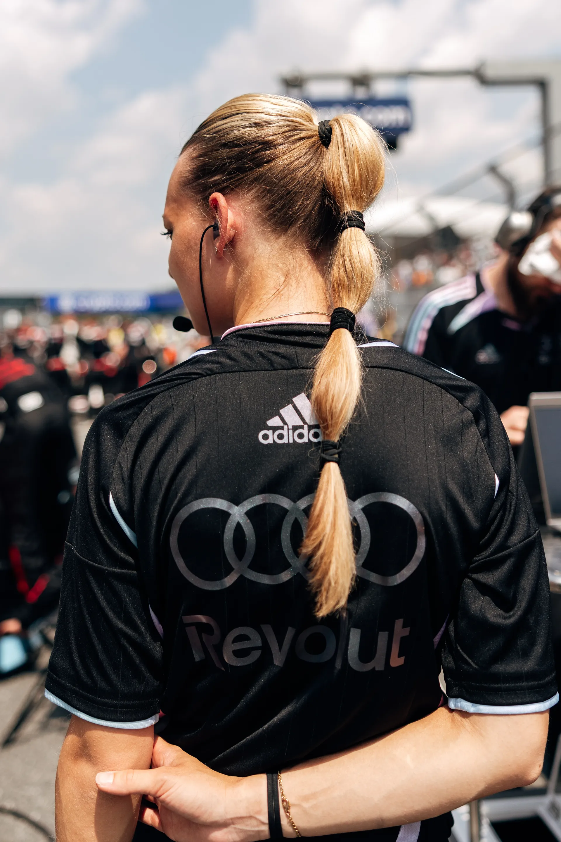 Rear view of a female Audi Revolut F1® Team crew member with a braided ponytail standing on the grid.
