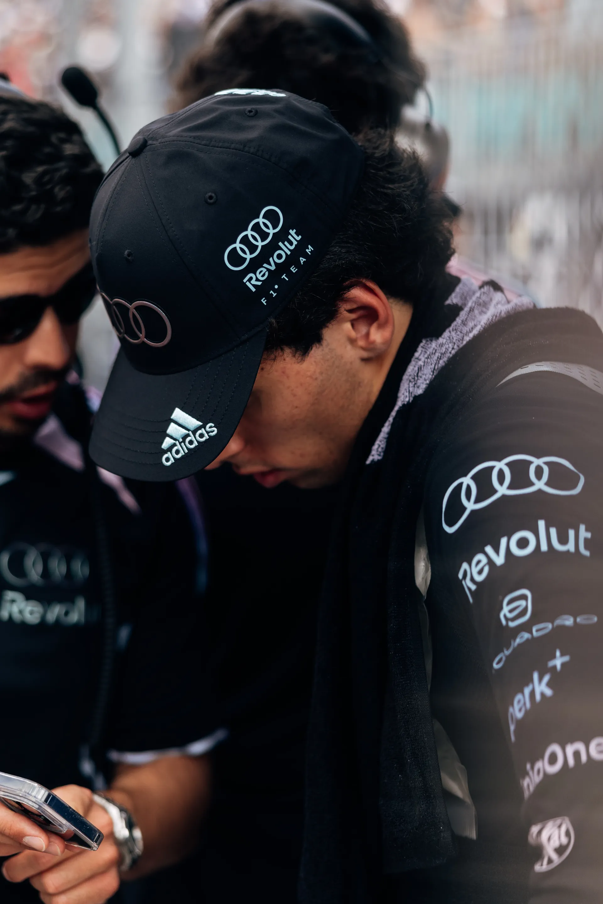 Gabriel Bortoleto looks down in concentration beside a team member while wearing an Audi Revolut F1® Team cap.