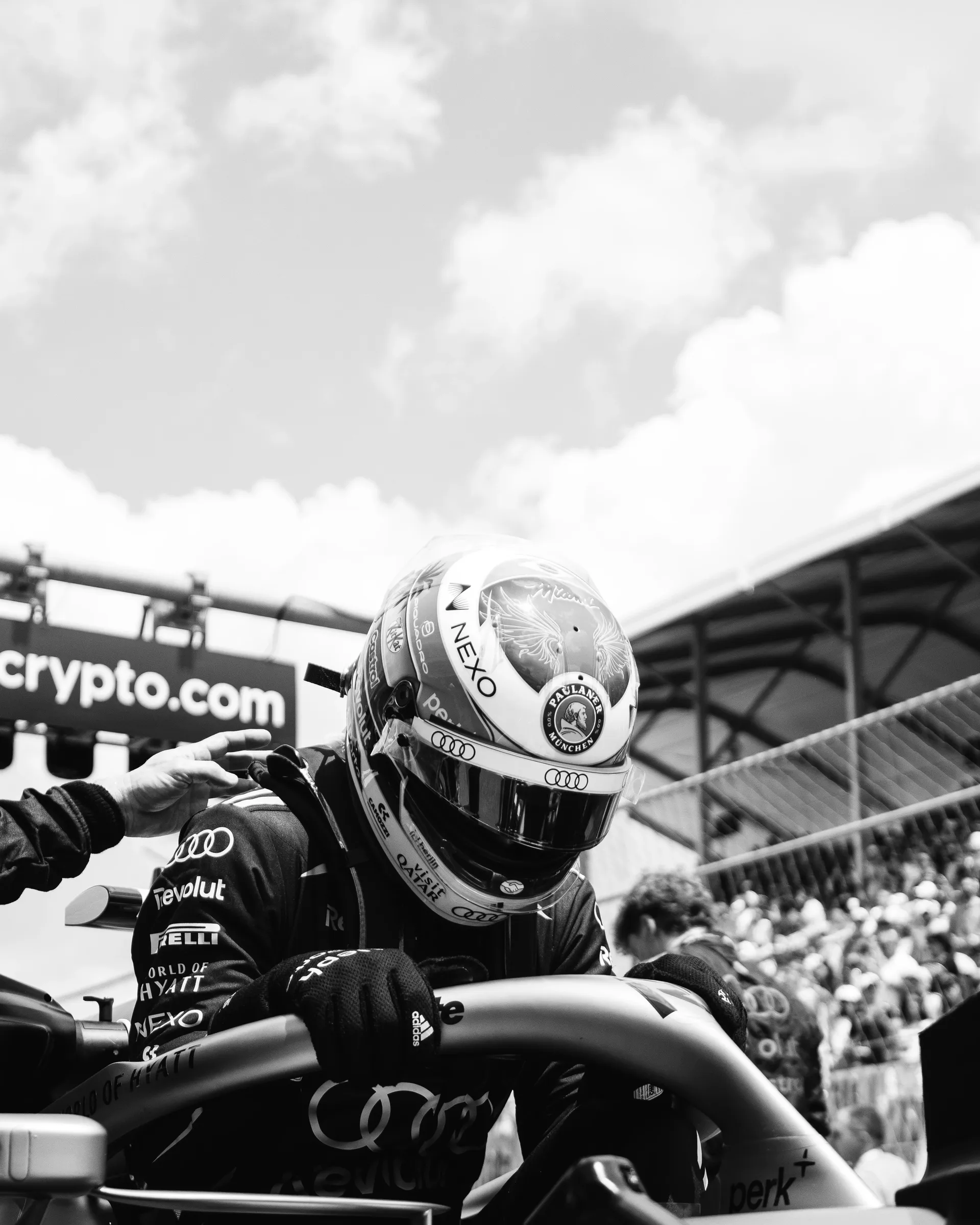 Black and white image of Gabriel Bortoleto seated low in the cockpit as a Audi Revolut F1® Team crew member places a hand on his shoulder.