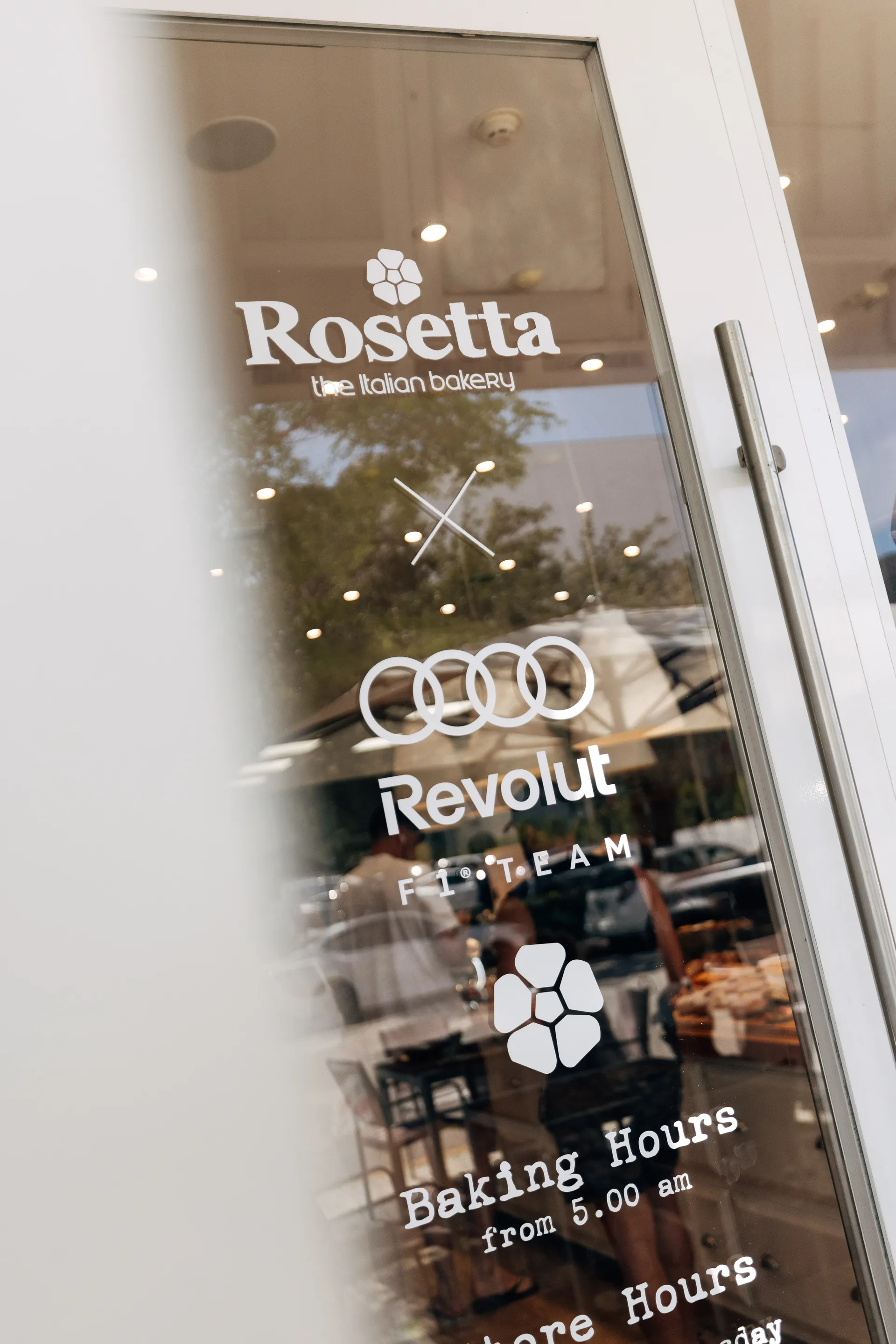 Glass door with Rosetta the Italian bakery and Audi Revolut F1® Team branding, photographed from outside with reflections of the interior.