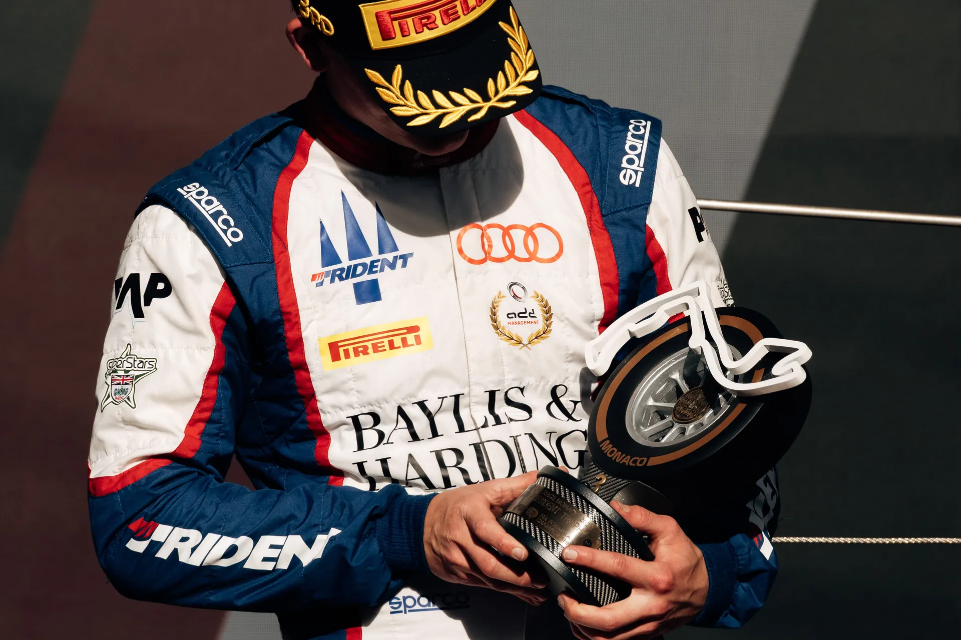 Freddie Slater holding his trophy on the podium in Monaco, Audi rings on his race suit