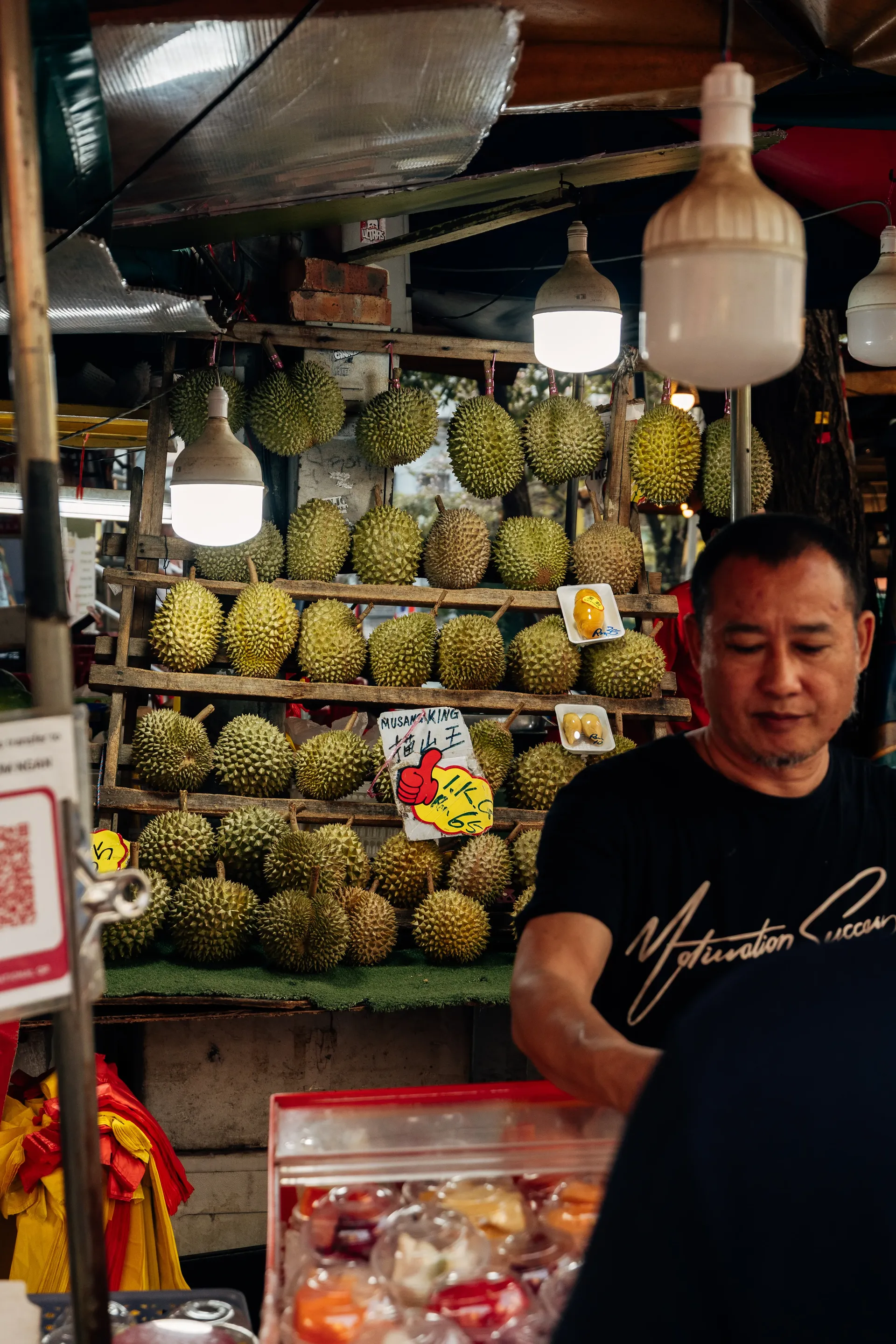 Vendor at a durian stall with rows of durians on wooden shelves in Kuala Lumpur