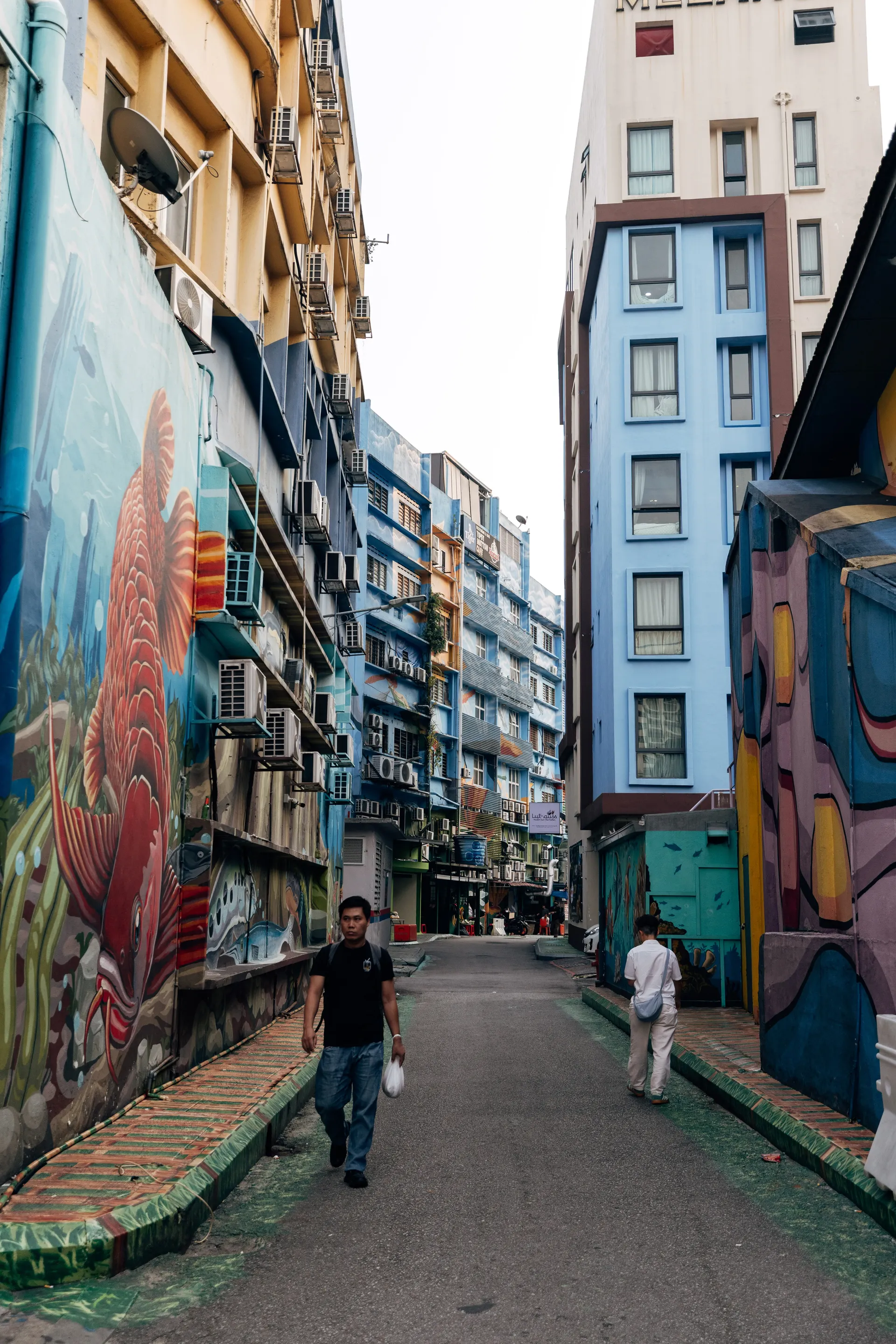 Pedestrians in a narrow alley with a large fish mural and painted buildings in Kuala Lumpur