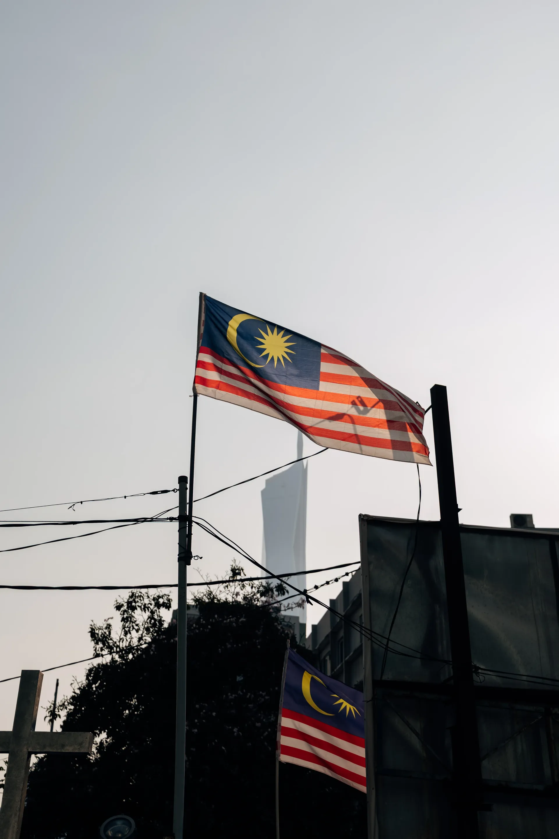 Two Malaysian flags on poles with a skyscraper in the haze behind, Kuala Lumpur