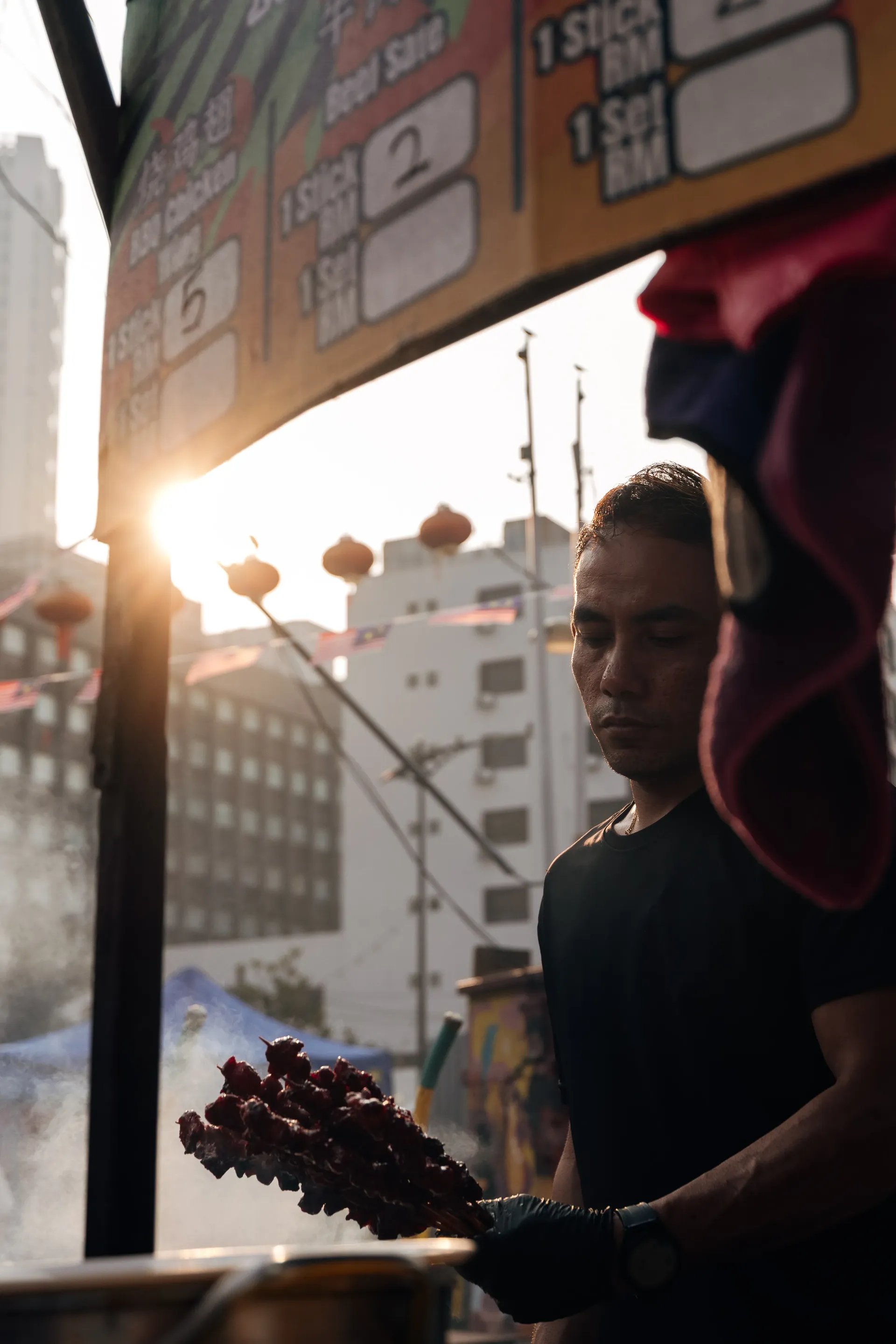 Street food vendor holding skewers at a stall in backlight in Kuala Lumpur