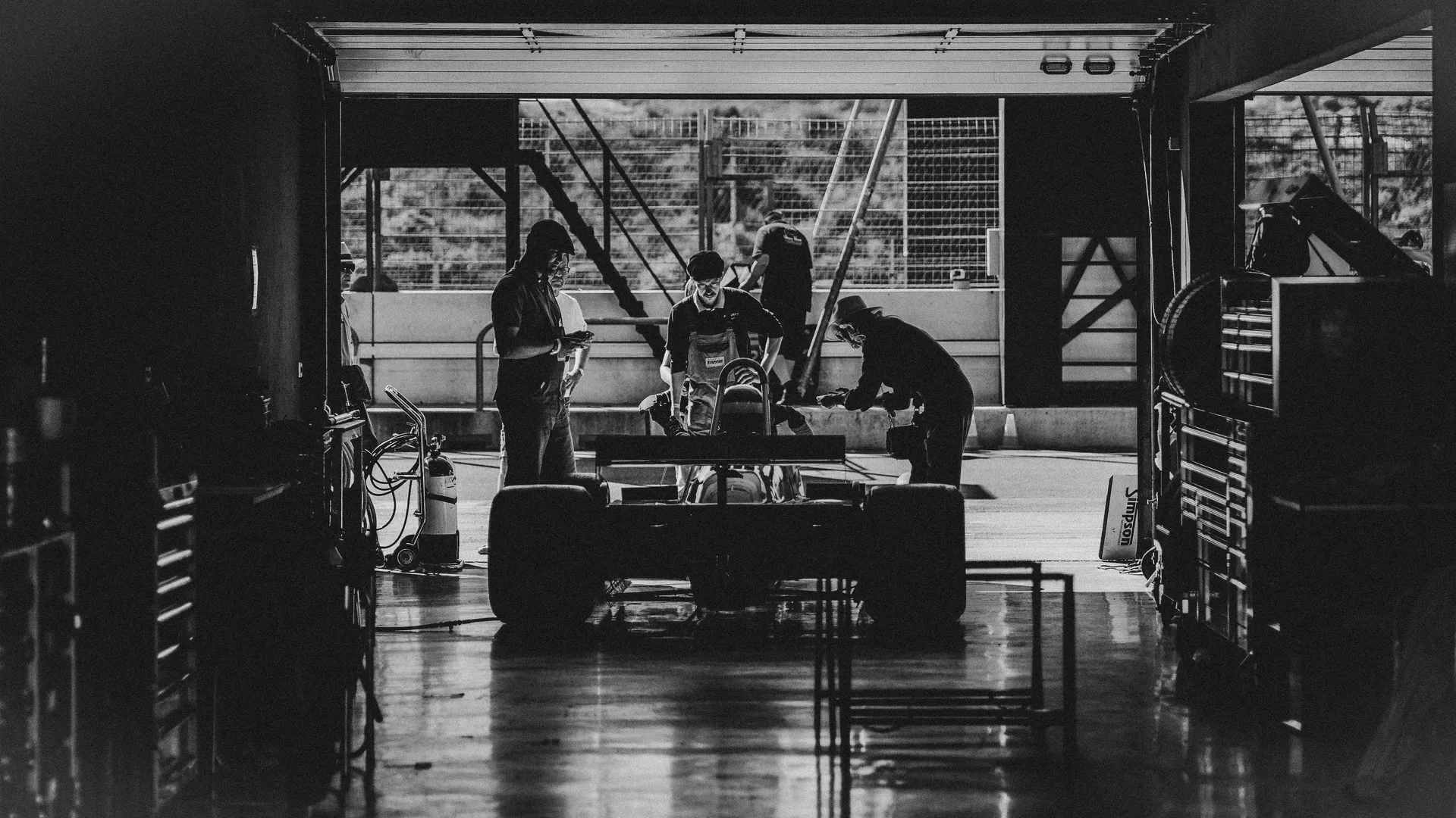 Black-and-white photo of mechanics prepping a vintage race car in the garage — Audi Revolut F1 Team pit crew energy