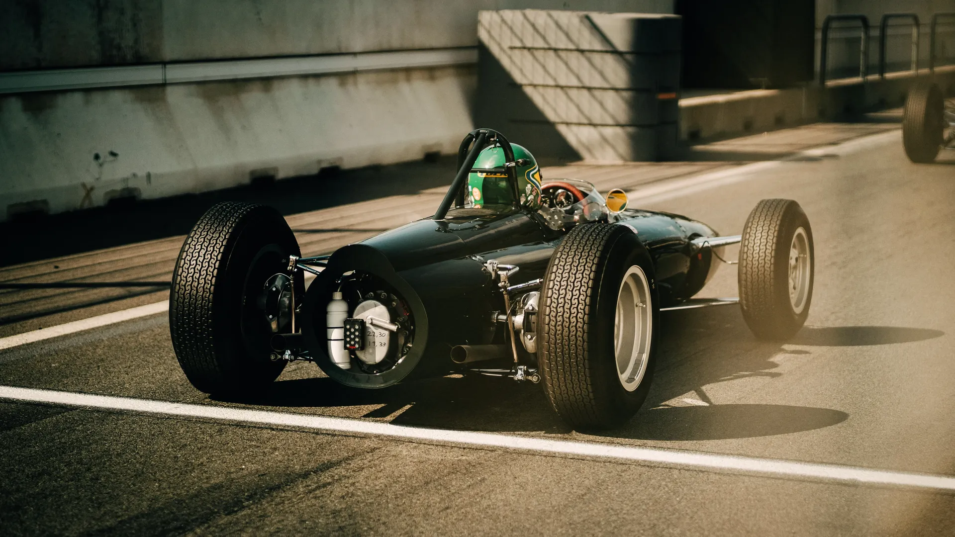 Vintage open-wheel race car with driver in a green helmet on track — Audi Revolut F1 Team historic racing heritage