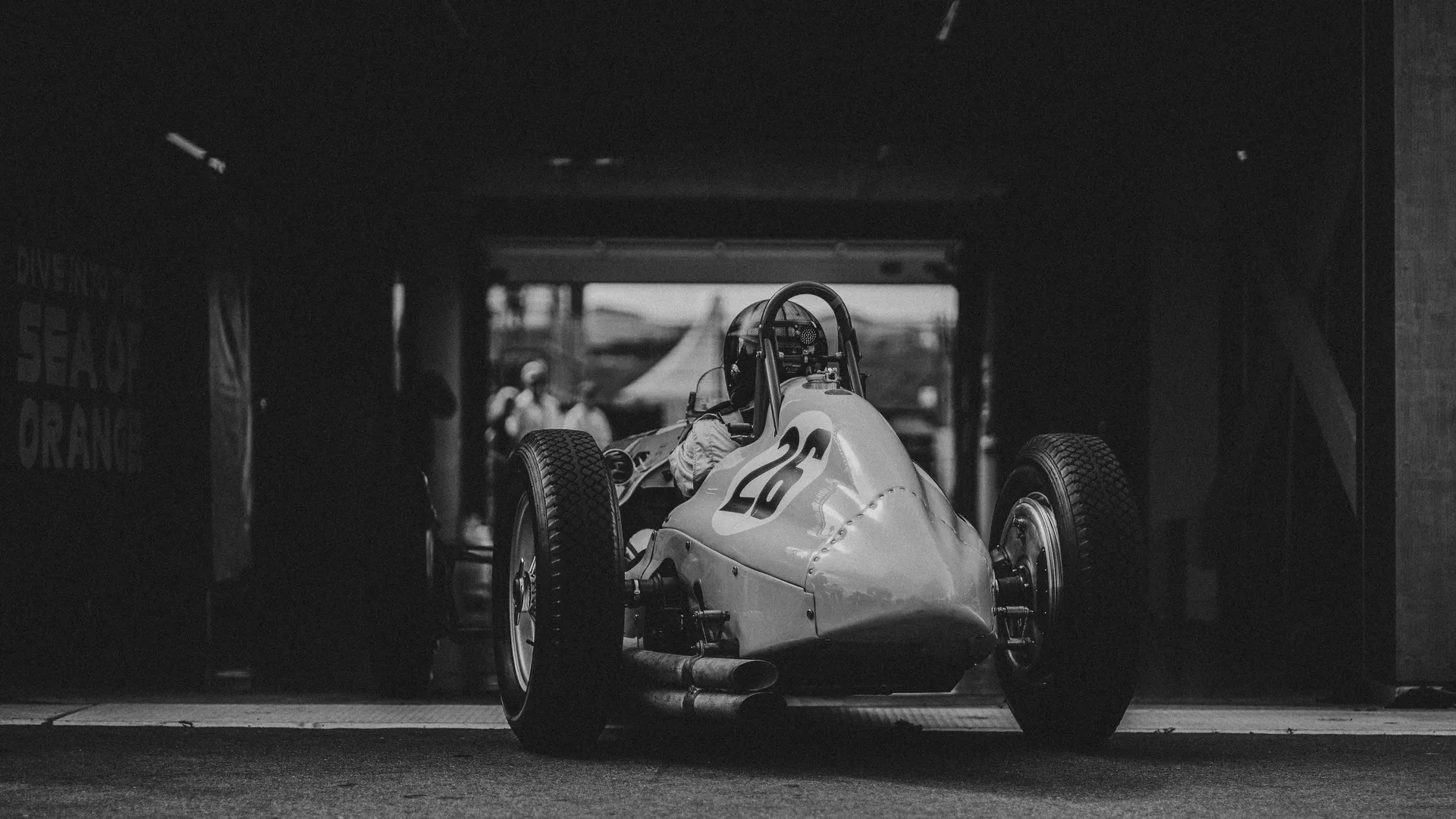 Vintage race car number 26 exiting a garage beneath a "Sea of Orange" sign — Audi Revolut F1 Team Dutch GP fan culture