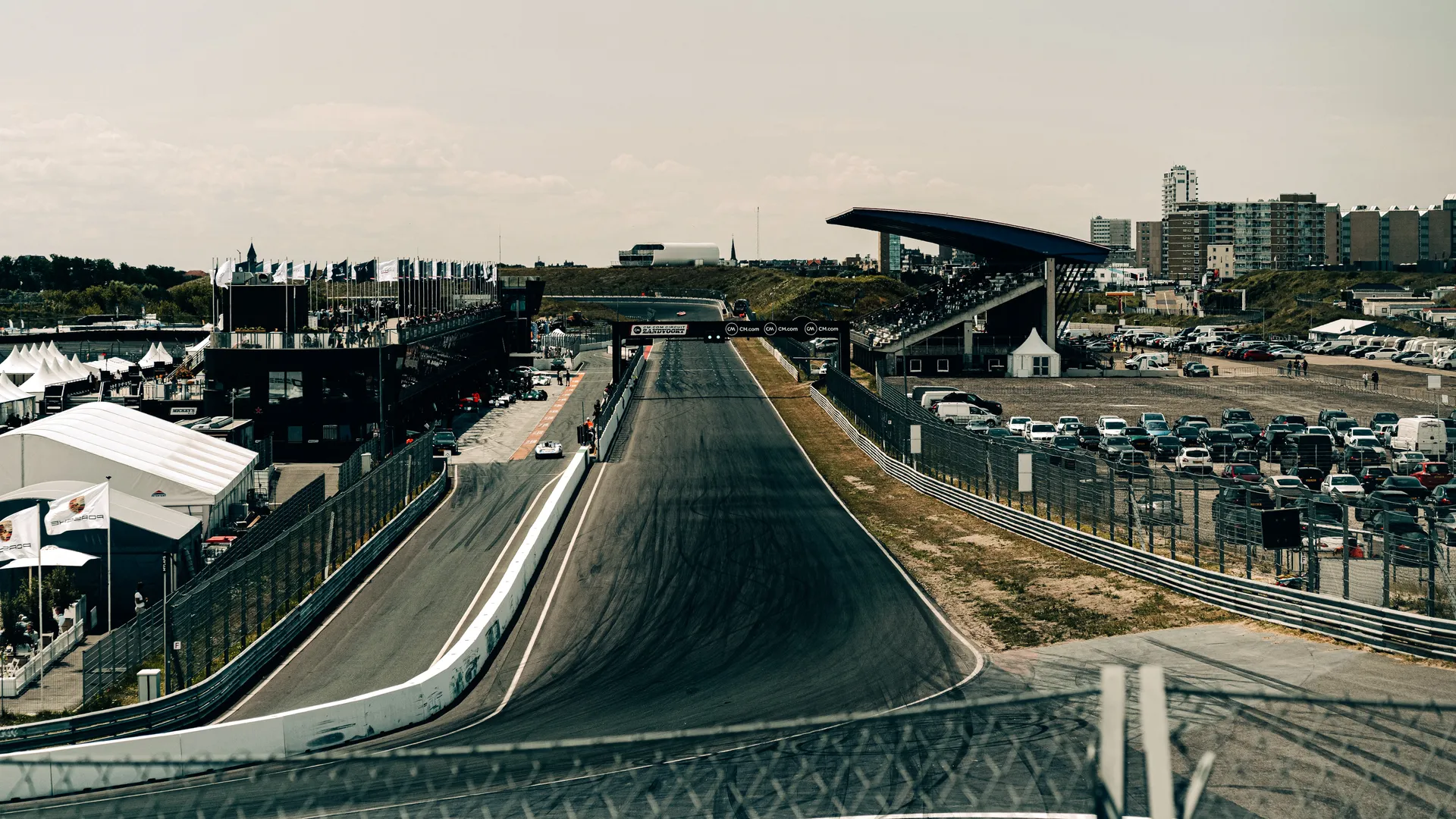 Elevated view across the main straight and pit lane at Circuit Zandvoort, with grandstands, paddock buildings and the surrounding coastal town.