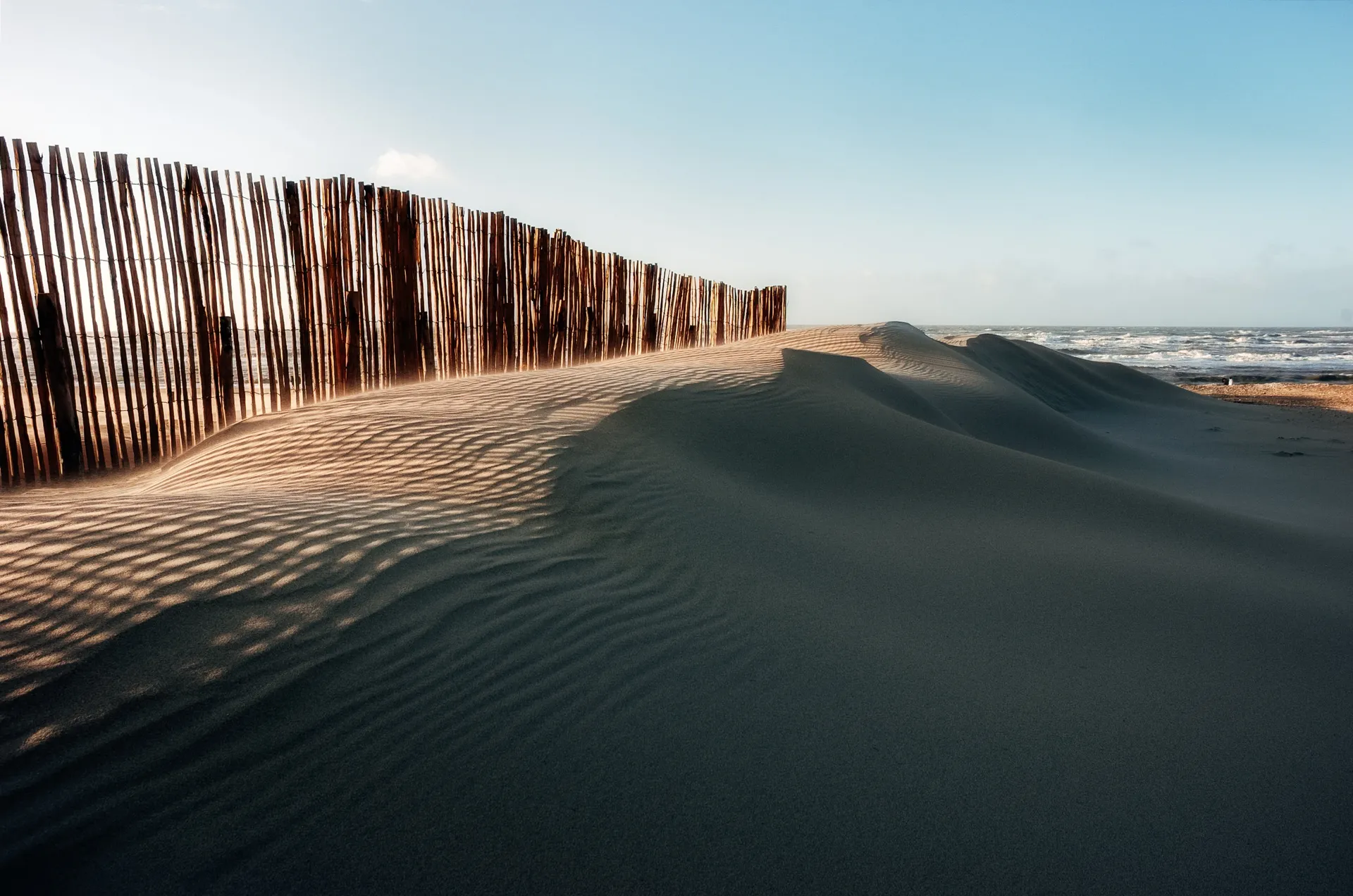 Windswept sand dunes beside the North Sea near Circuit Zandvoort, with wooden fencing casting shadows across the sand.