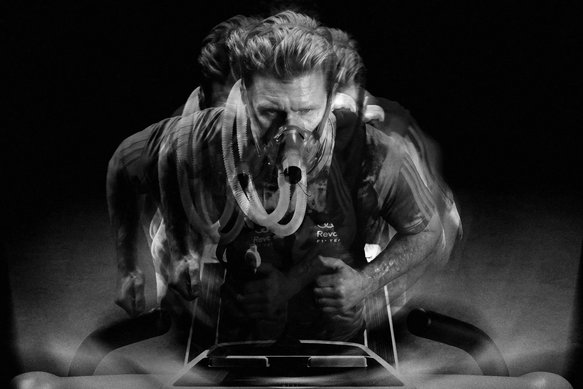 Black-and-white portrait of Nico Hulkenberg, driver for the Audi Revolut F1® Team, wearing a balaclava and captured with multiple-exposure motion blur under a spotlight.