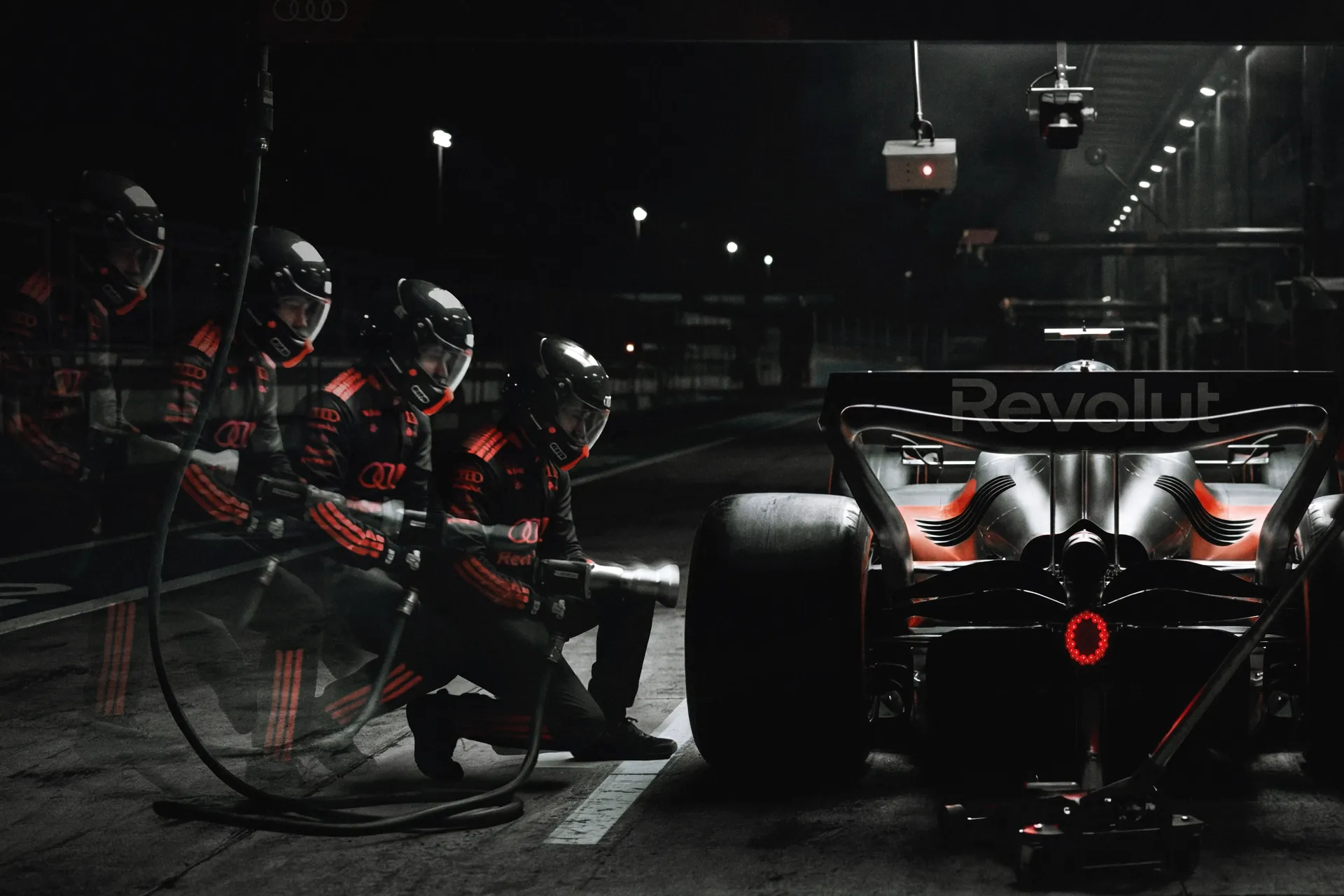 The Audi R26 during a nighttime pit stop, surrounded by the Audi Revolut F1® Team pit crew captured with multiple-exposure motion blur.