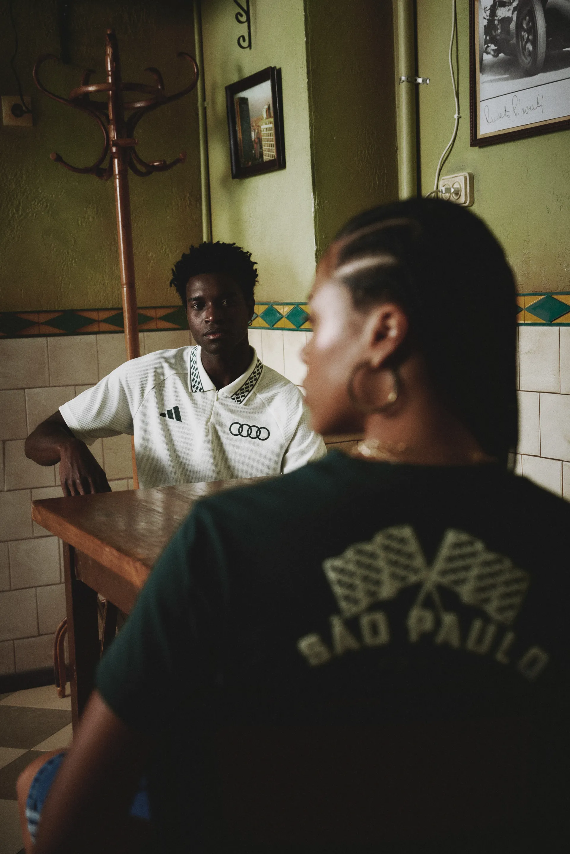Rear view of a model in a green São Paulo flag T-shirt in a café, adidas x Audi Revolut F1® Team Sampa Soul collection