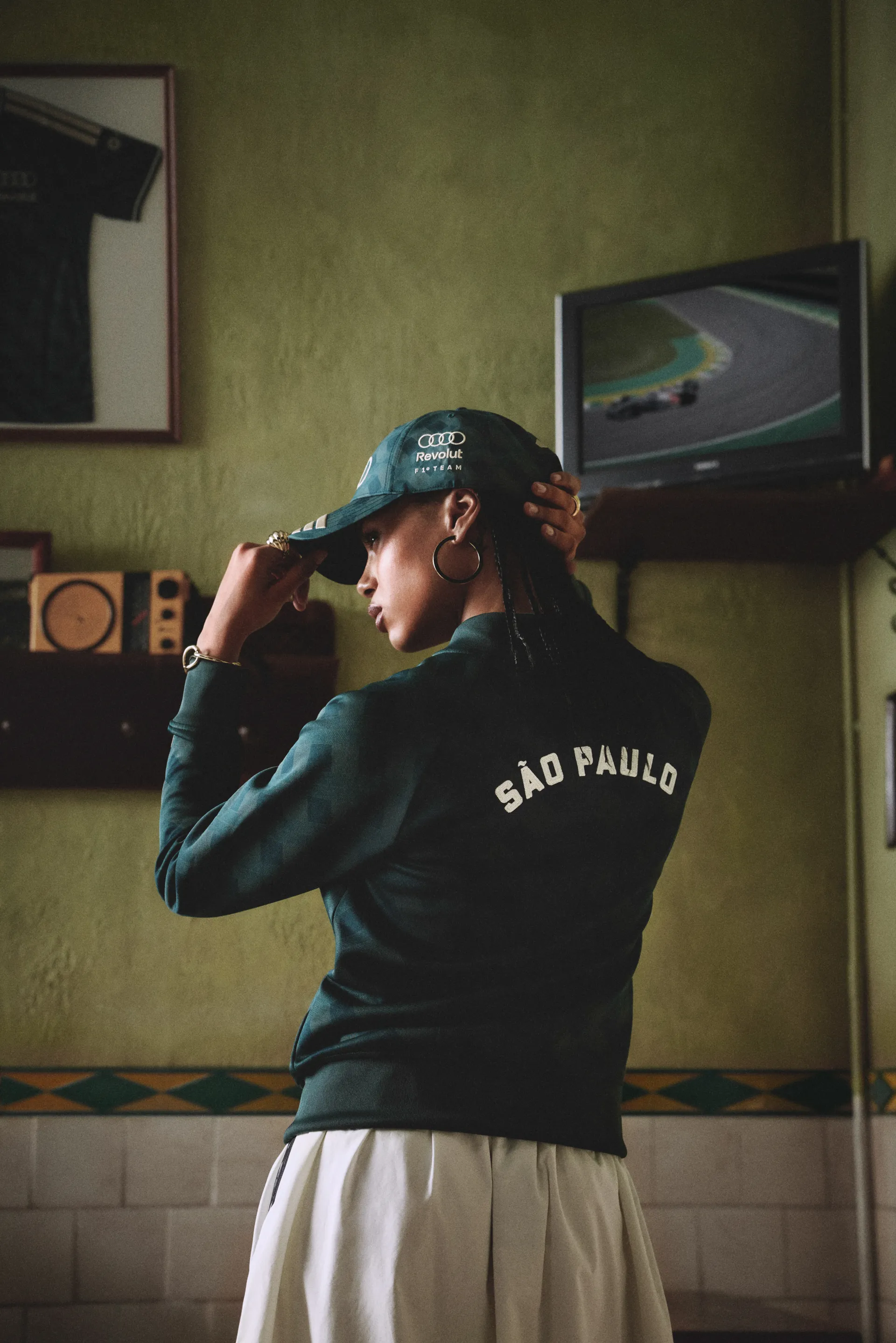 Model adjusting a green cap, São Paulo track jacket from behind, adidas x Audi Revolut F1® Team Sampa Soul collection