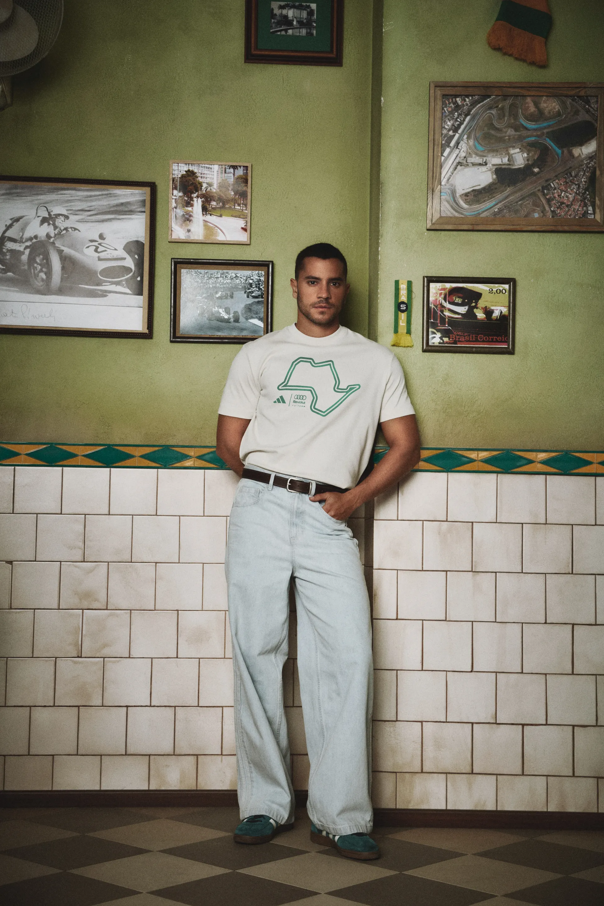 Model in a white graphic T-shirt and light jeans by a tiled café wall, adidas x Audi Revolut F1® Team Sampa Soul collection