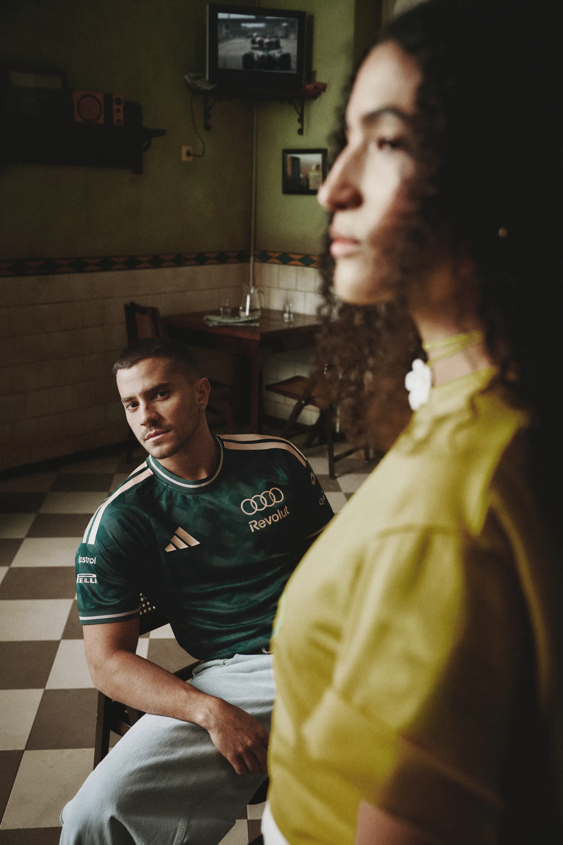 Model in a green team jersey seated behind a model in yellow, adidas x Audi Revolut F1® Team Sampa Soul collection