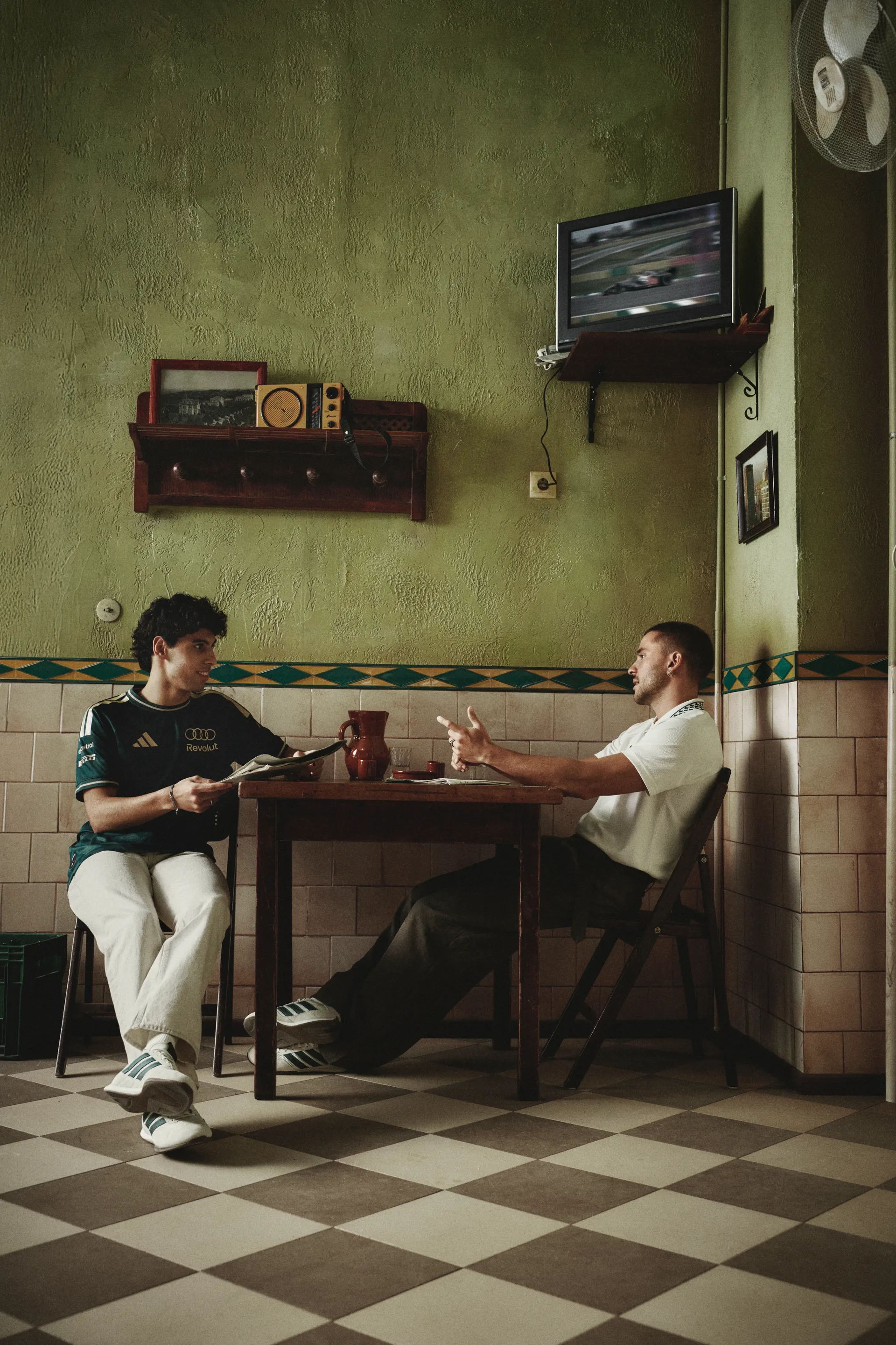 Audi Revolut F1® Team driver Gabriel Bortoleto and a male model at a café table in a green jersey and white T-shirt, adidas x Audi Revolut F1® Team Sampa Soul collection