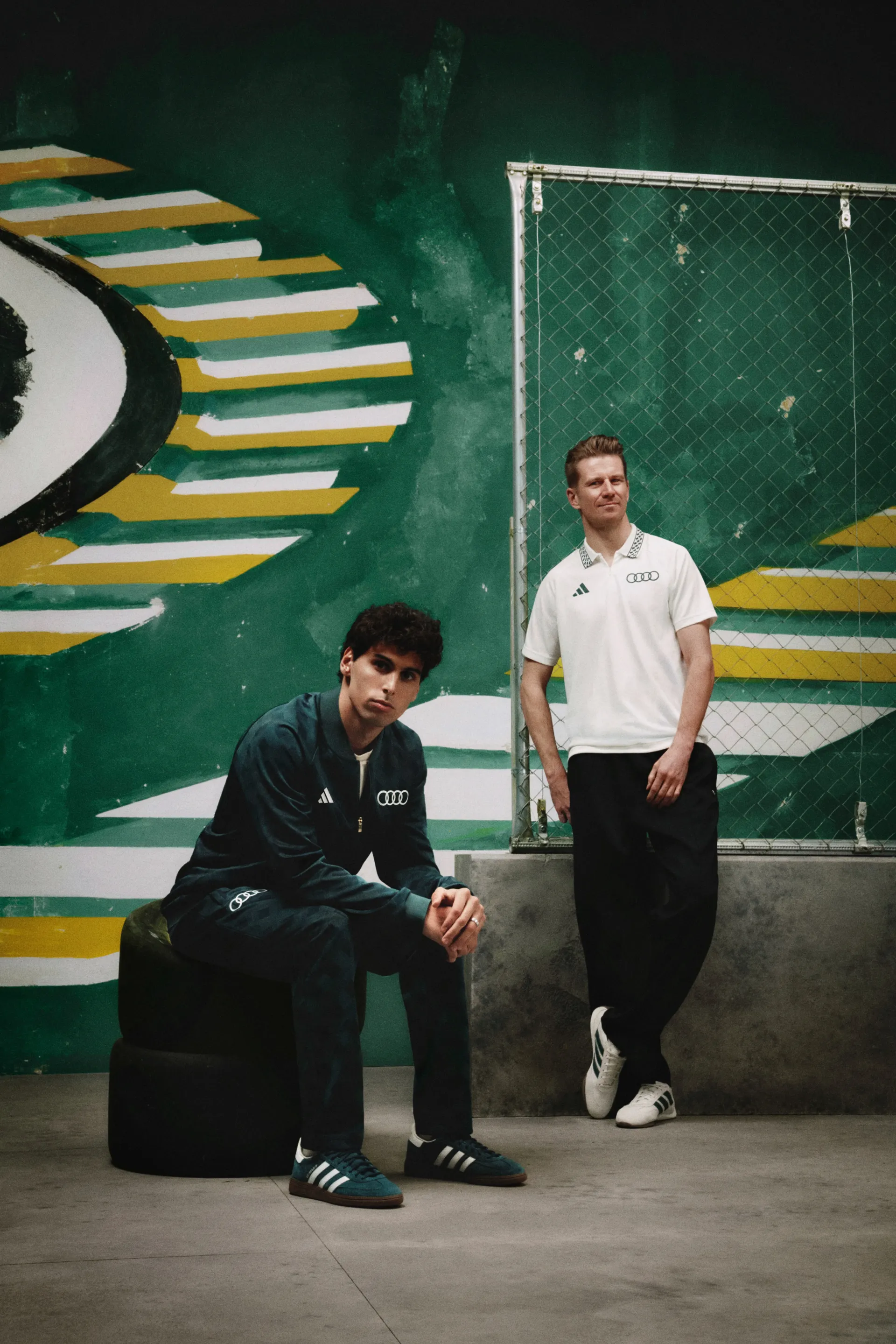 Nico Hulkenberg and Gabriel Bortoleto drivers at the Audi Revolut F1® Team side by side in front of a green and yellow mural, adidas x Audi Revolut F1® Team Sampa Soul collection