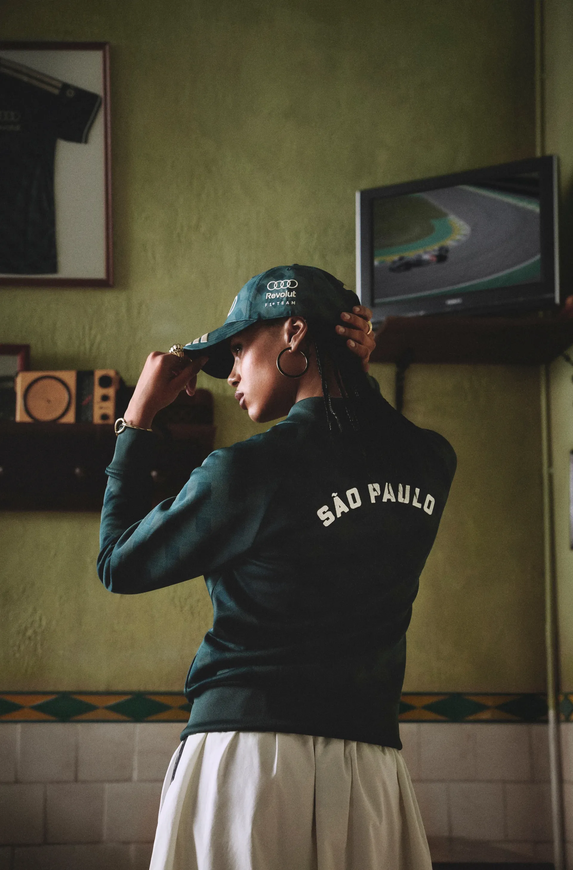 Rear view of a model in the adidas x Audi Revolut F1® Team jacket with São Paulo lettering, adjusting a matching cap