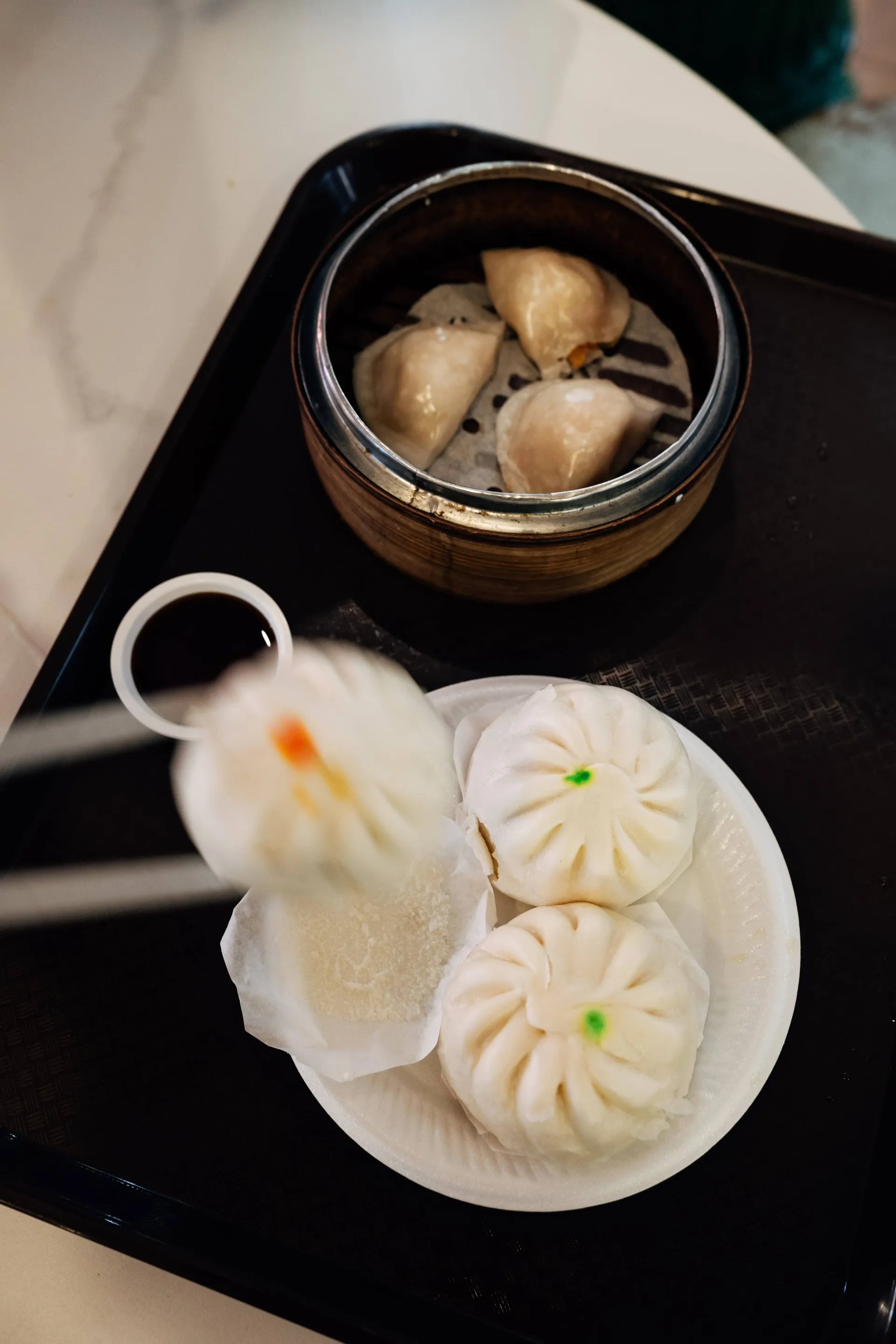 Dim sum with steamed buns, dumplings in a bamboo steamer and soy sauce on a tray in Singapore