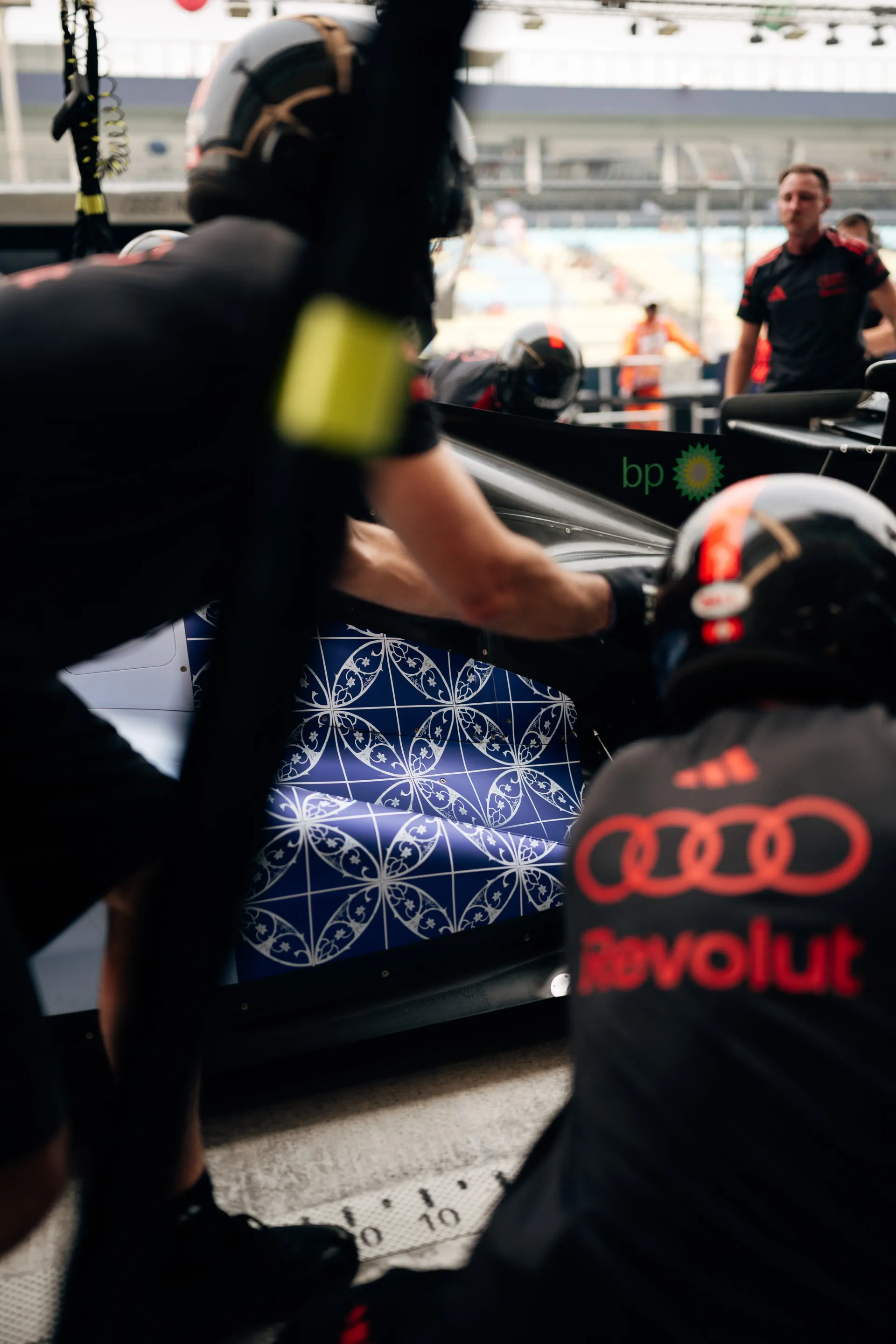 Audi Revolut F1® Team mechanics working on the car in the pit lane, the blue patterned sidepod livery visible between them.