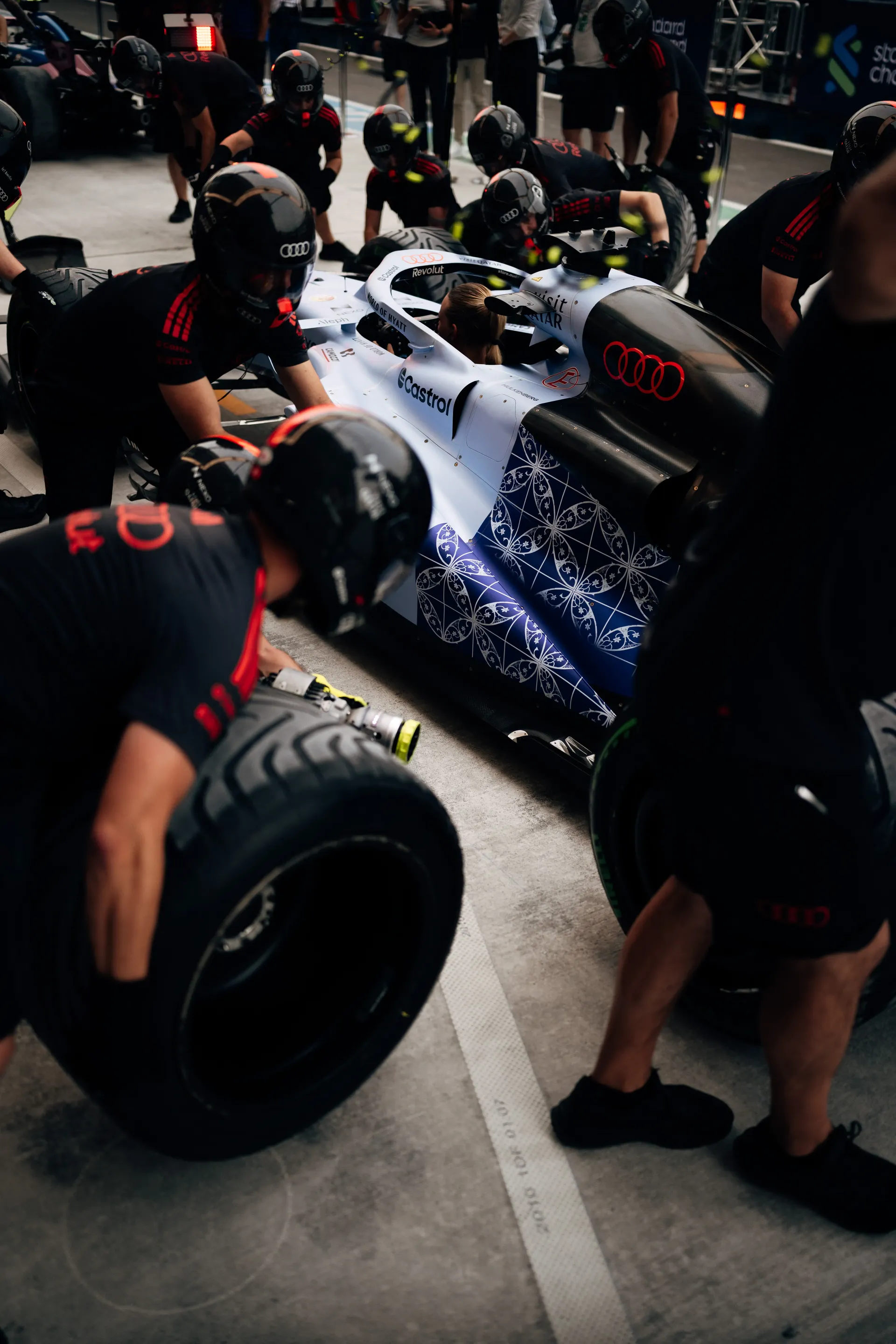 Audi Revolut F1® Team mechanics in pit crew helmets changing tyres on the white and blue car during pit stop practice.