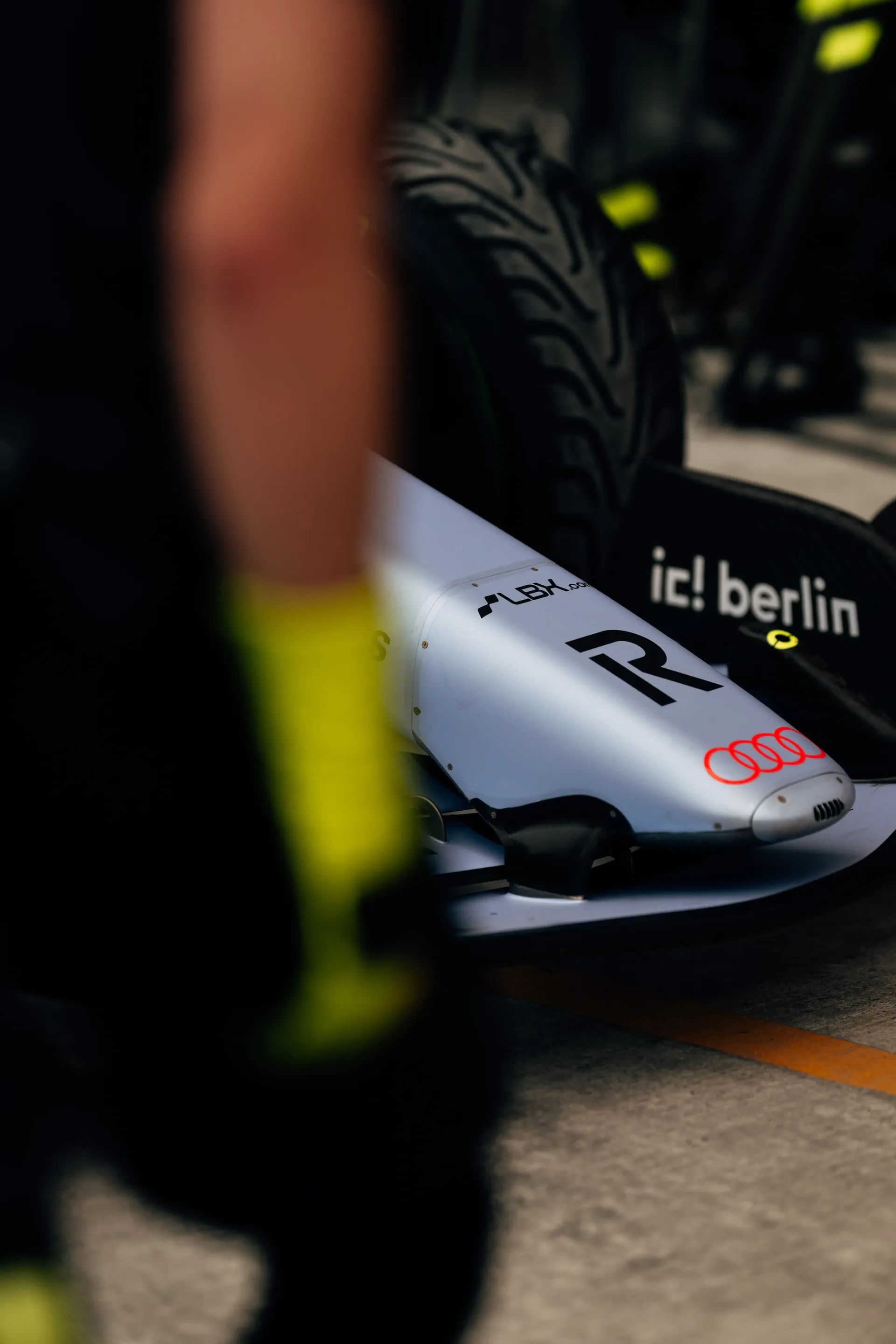 Close-up of the Audi Revolut F1® Team car’s nose with Audi rings and ic! berlin branding, a mechanic blurred in the foreground.