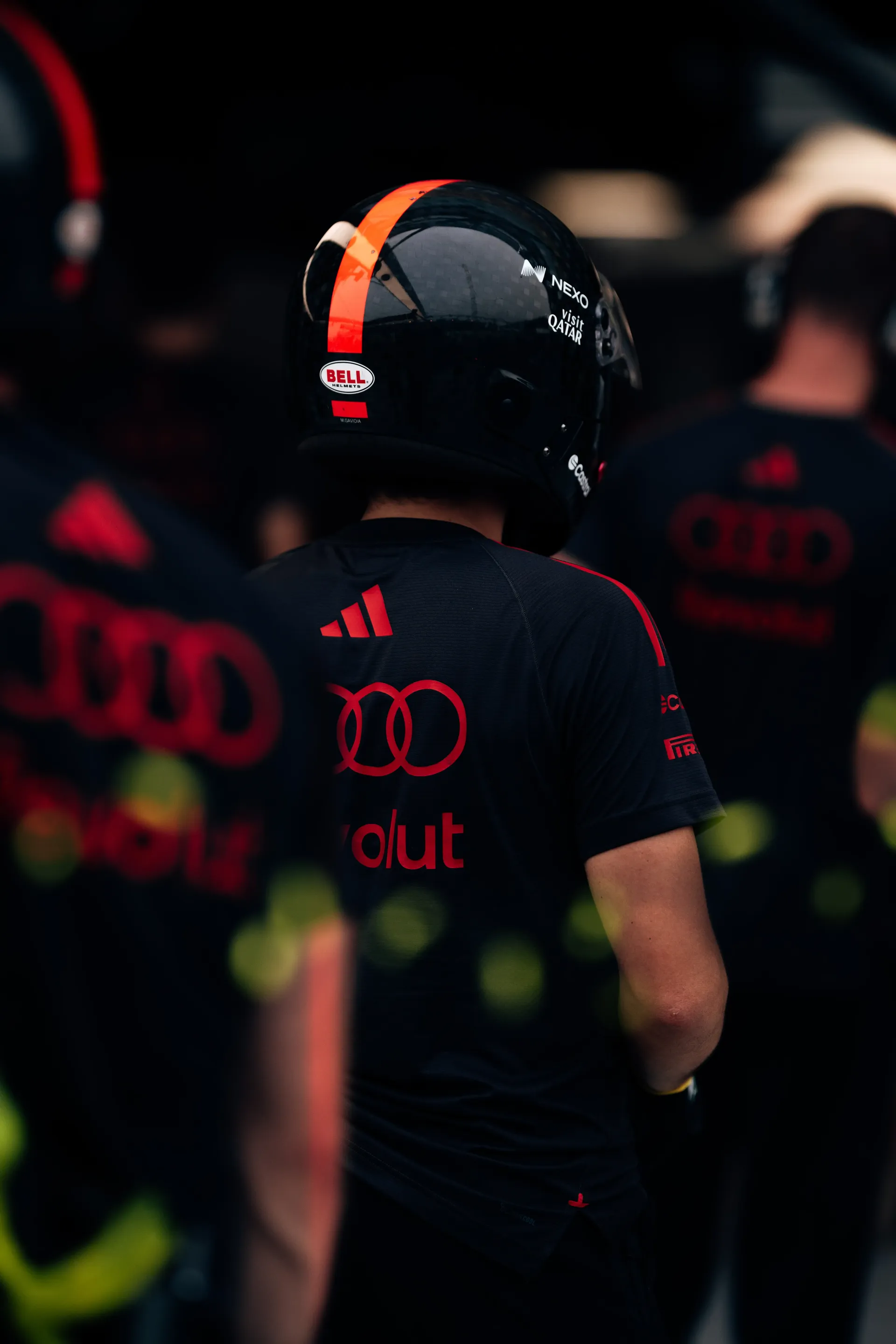 Audi Revolut F1® Team mechanic in a black pit crew helmet with an orange stripe, seen from behind among the crew.