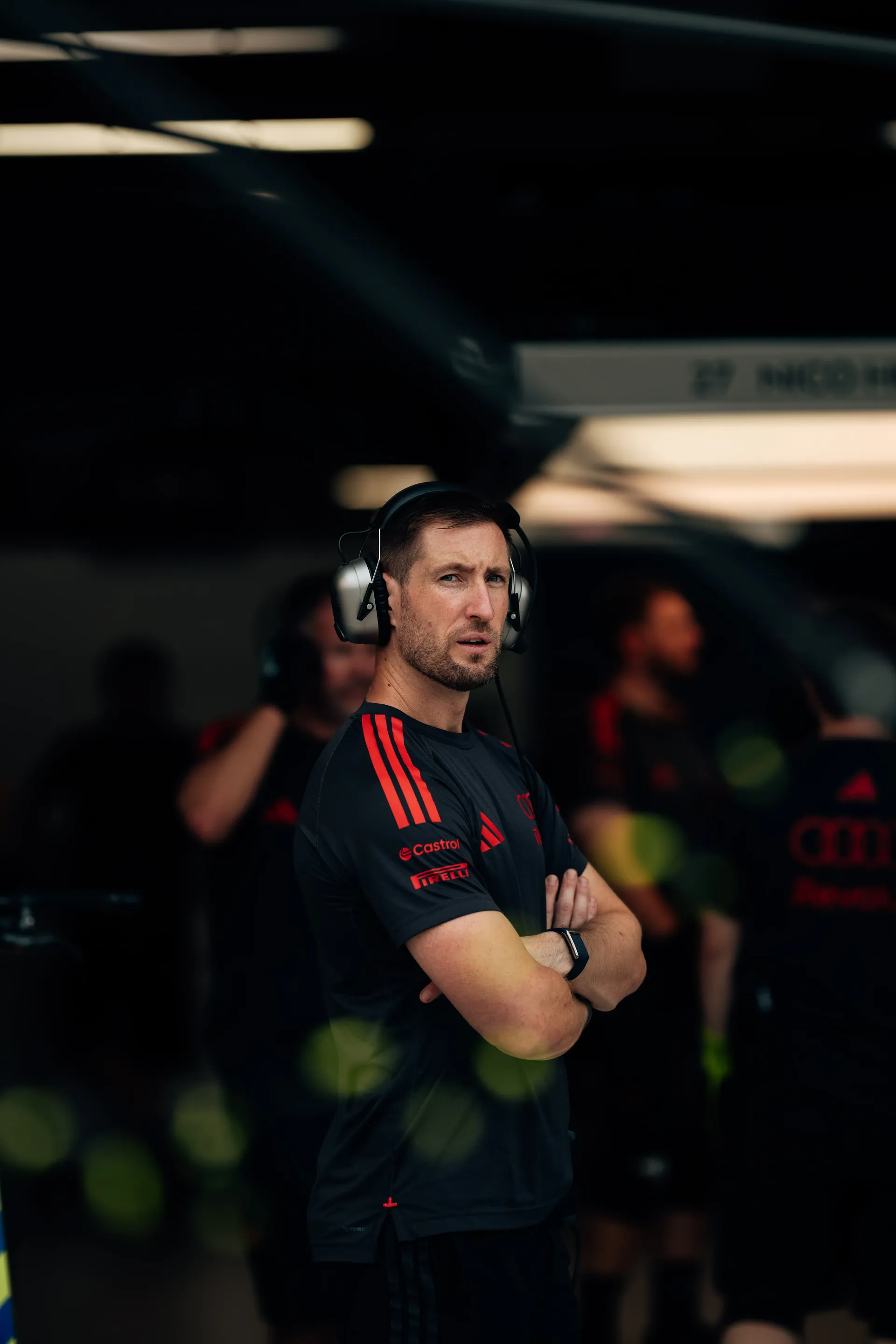 Audi Revolut F1® Team mechanic wearing a headset, standing with arms crossed in the garage.