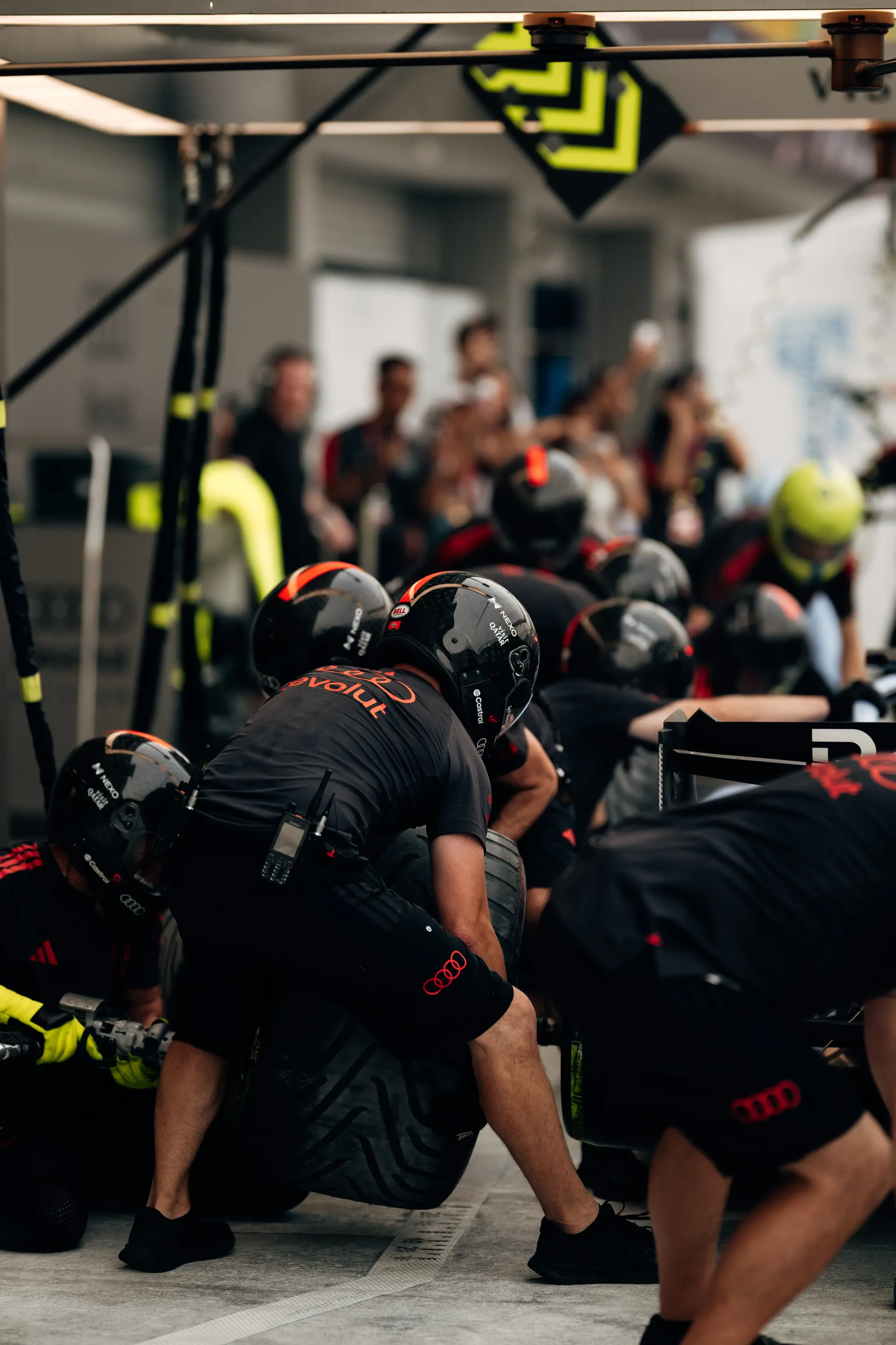 Audi Revolut F1® Team mechanics crouched around a tyre in the pit box during pit stop practice.