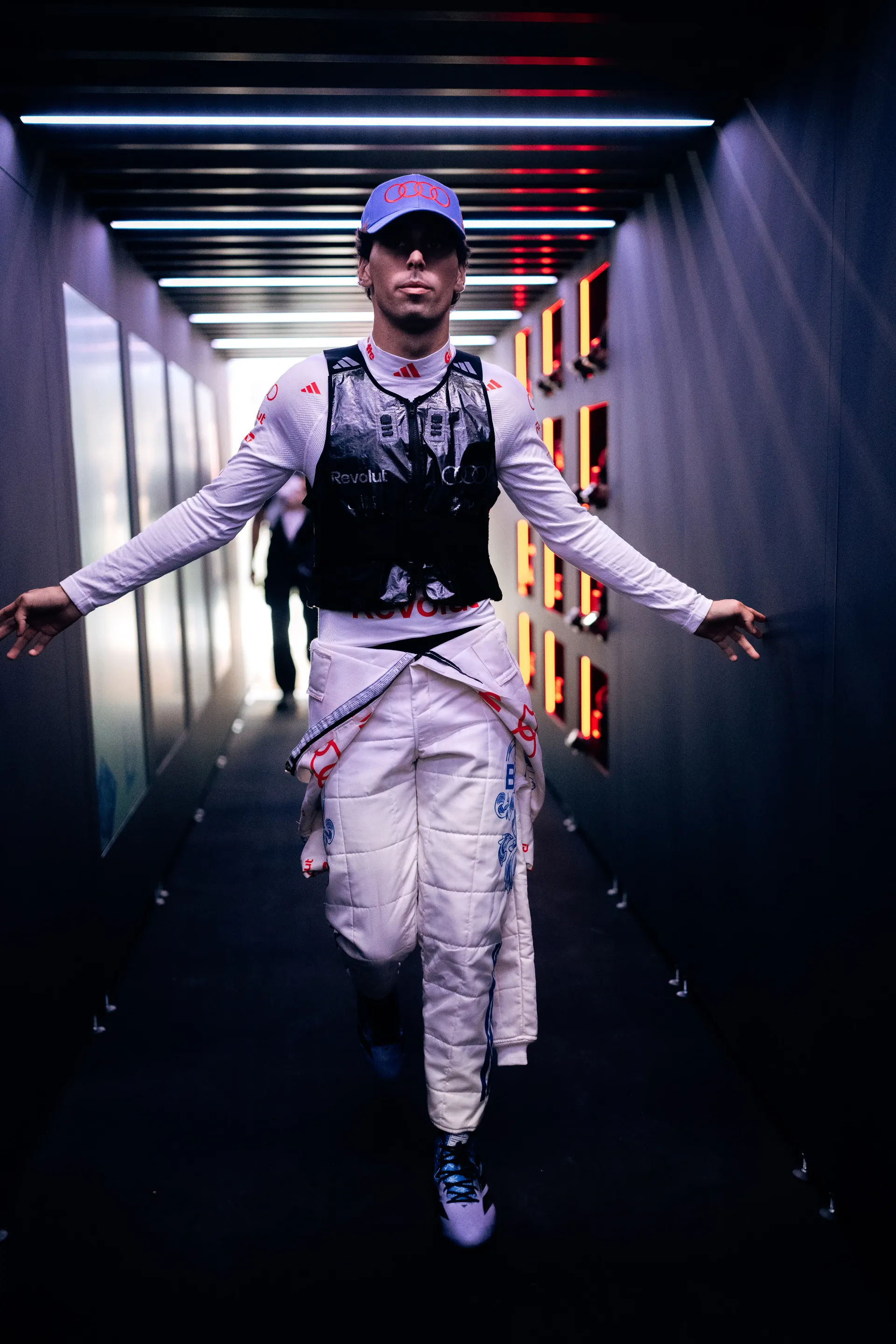 Gabriel Bortoleto of the Audi Revolut F1® Team walking through a lit tunnel in a cooling vest and cap, arms outstretched.