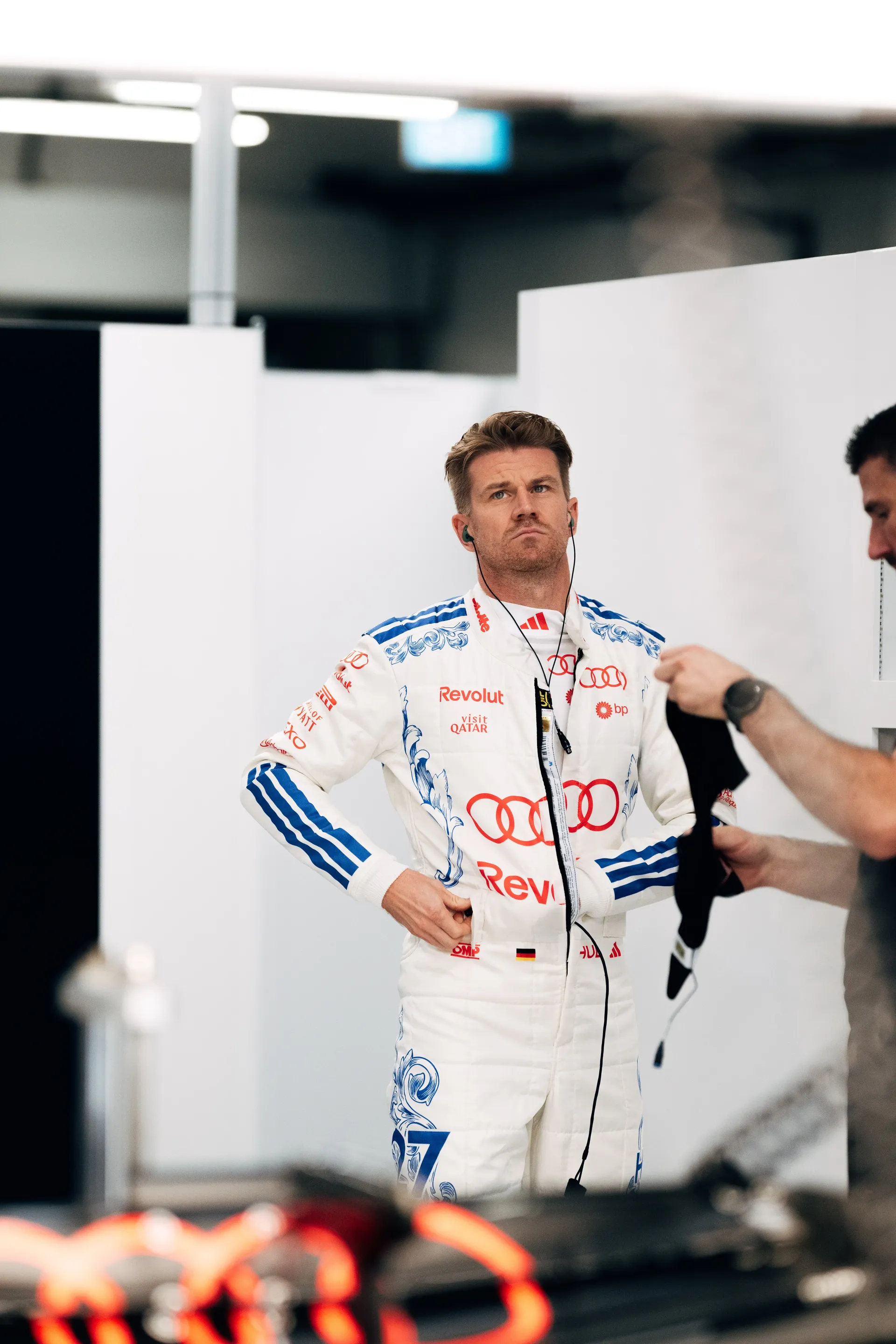 Nico Hulkenberg of the Audi Revolut F1® Team in his white race suit, hands on hips, in the garage.