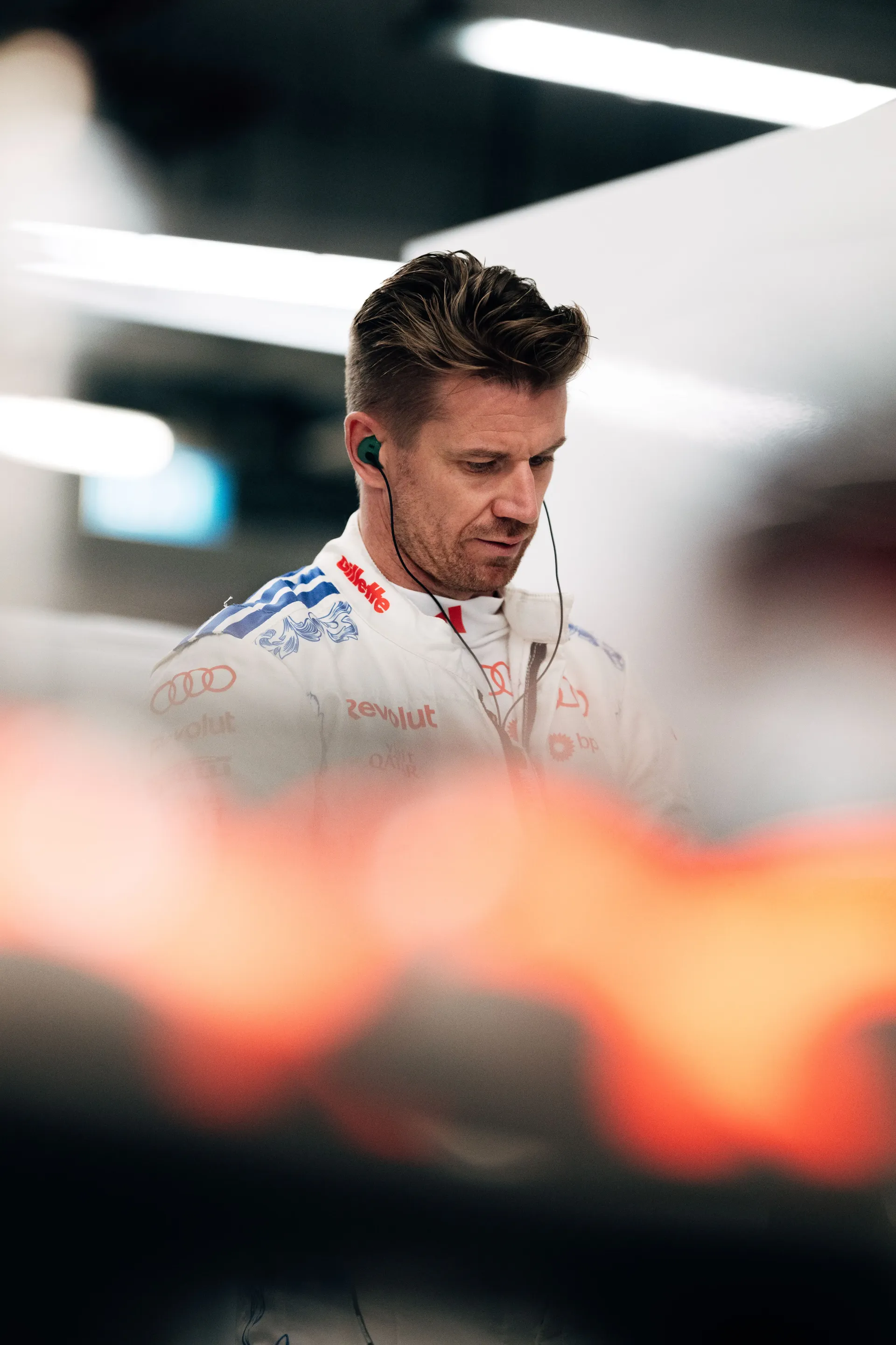 Nico Hulkenberg of the Audi Revolut F1® Team looking down in the garage, wearing earpieces and his white race suit.