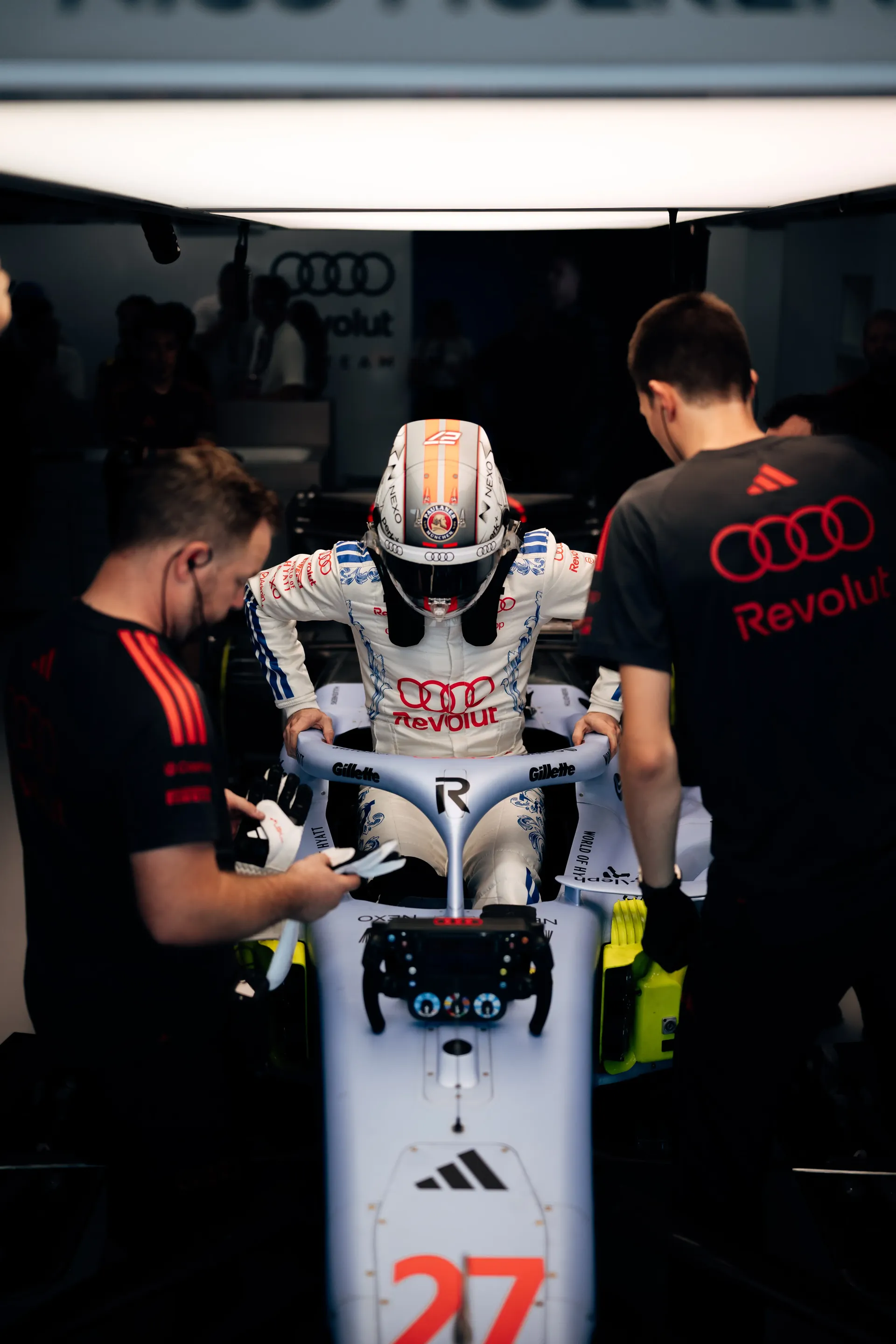 Nico Hulkenberg climbing into the Audi Revolut F1® Team car number 27, two mechanics standing either side.