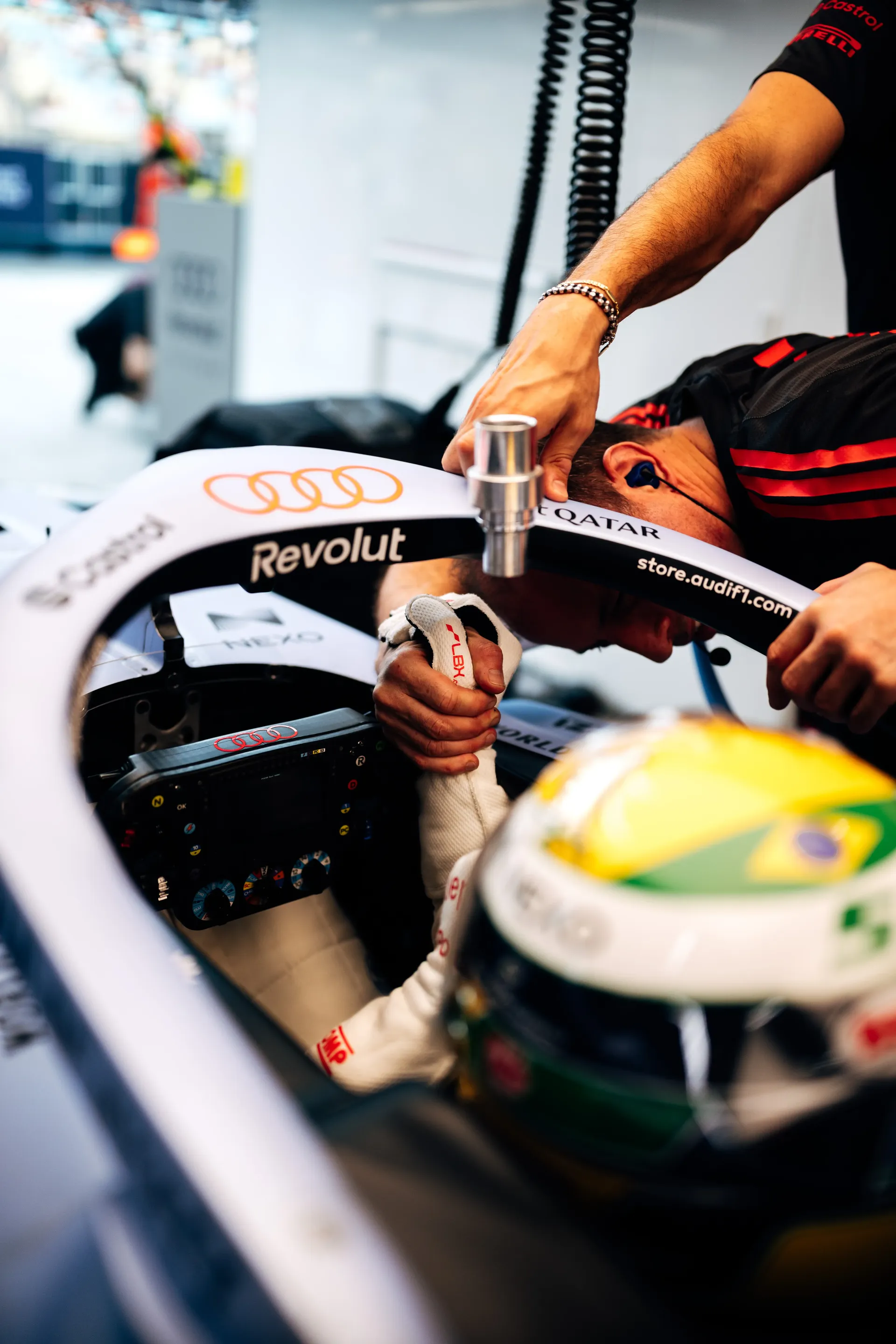 Audi Revolut F1® Team mechanic adjusting the cockpit as Gabriel Bortoleto sits in the car in his green and yellow helmet.
