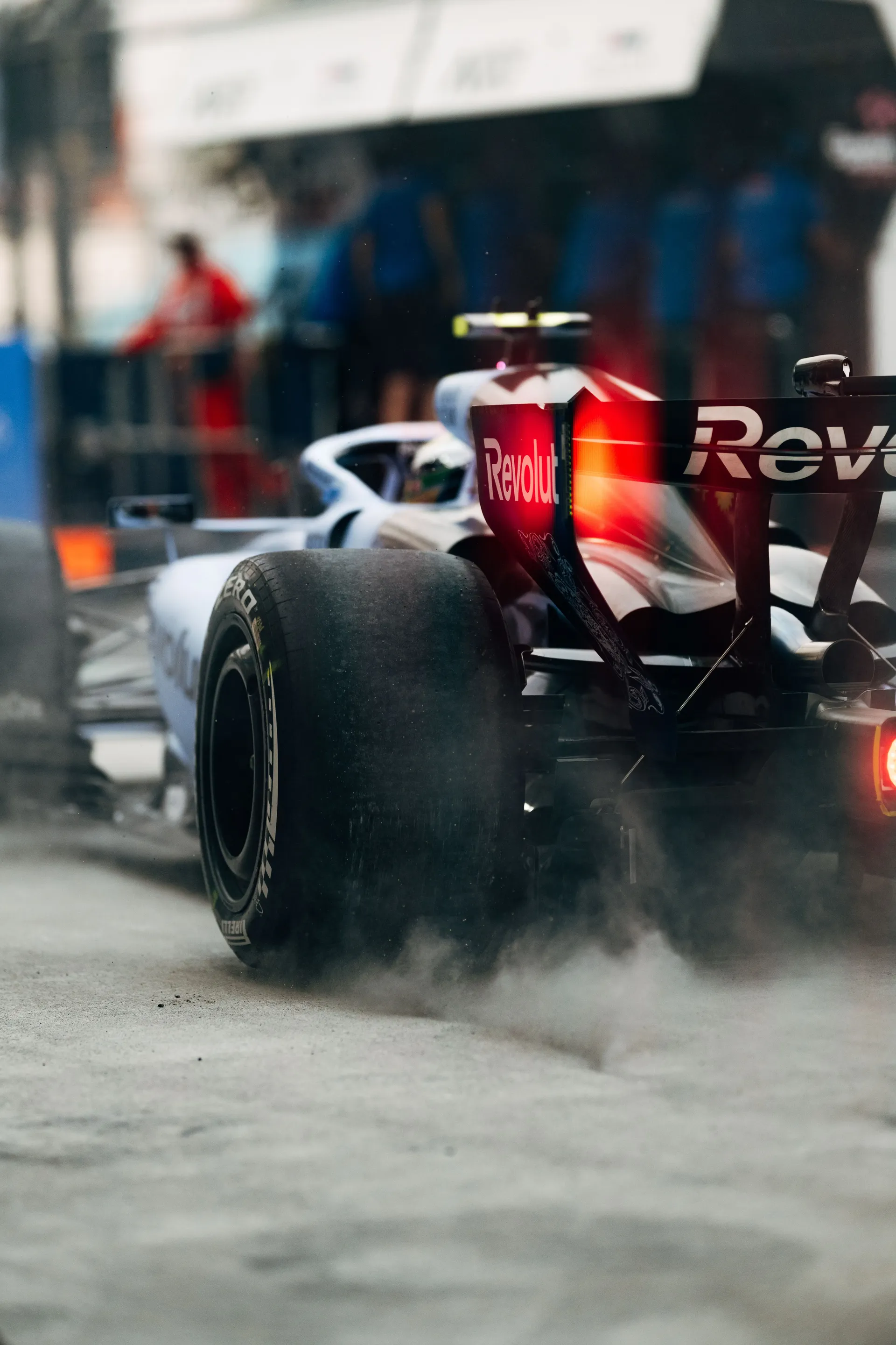 Audi Revolut F1® Team car R26 pulling away from the pit box with tyre smoke, mechanics watching.