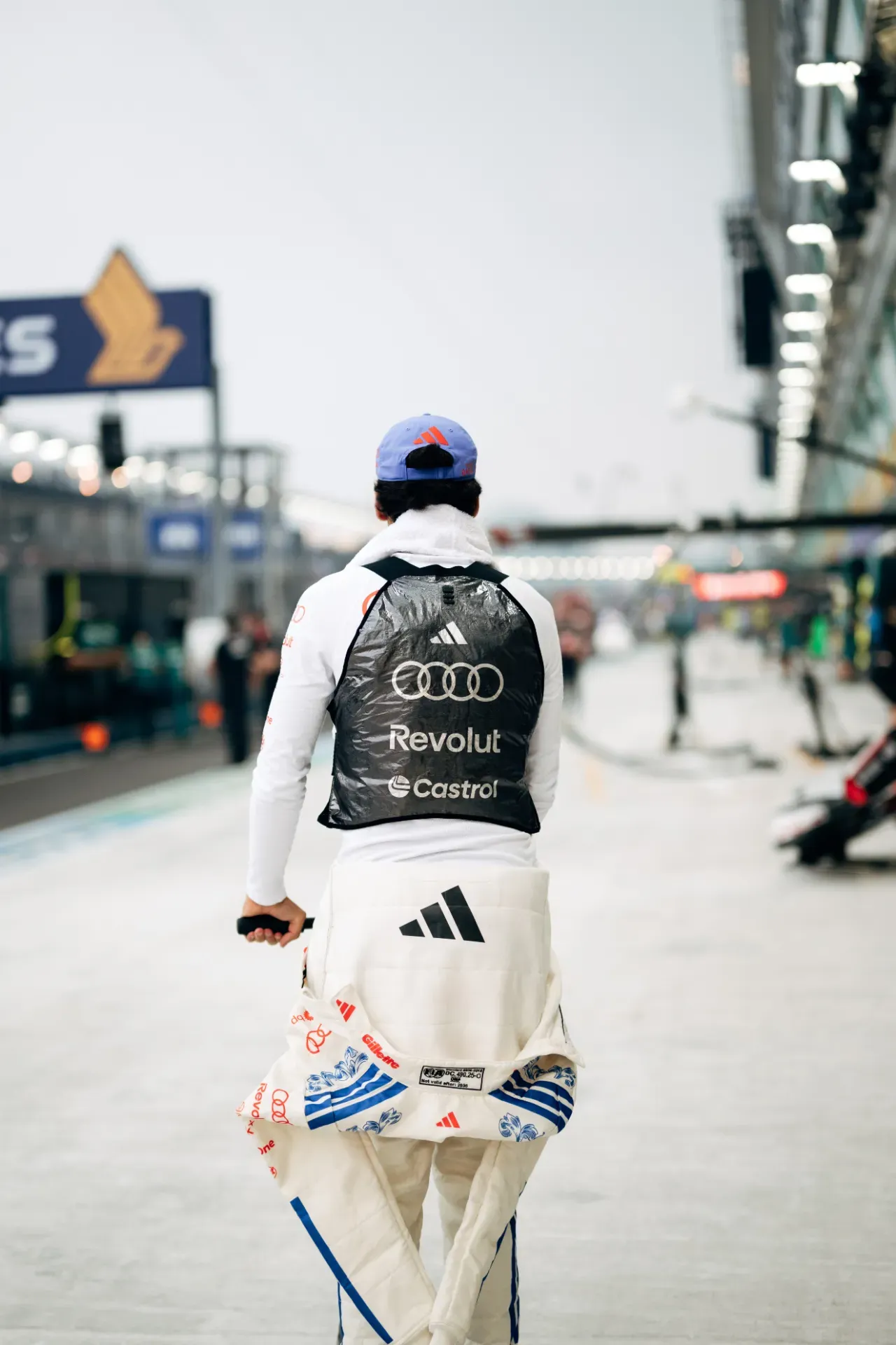 Gabriel Bortoleto of the Audi Revolut F1® Team in a cap and cooling vest walking along the pit lane in Singapore, from behind