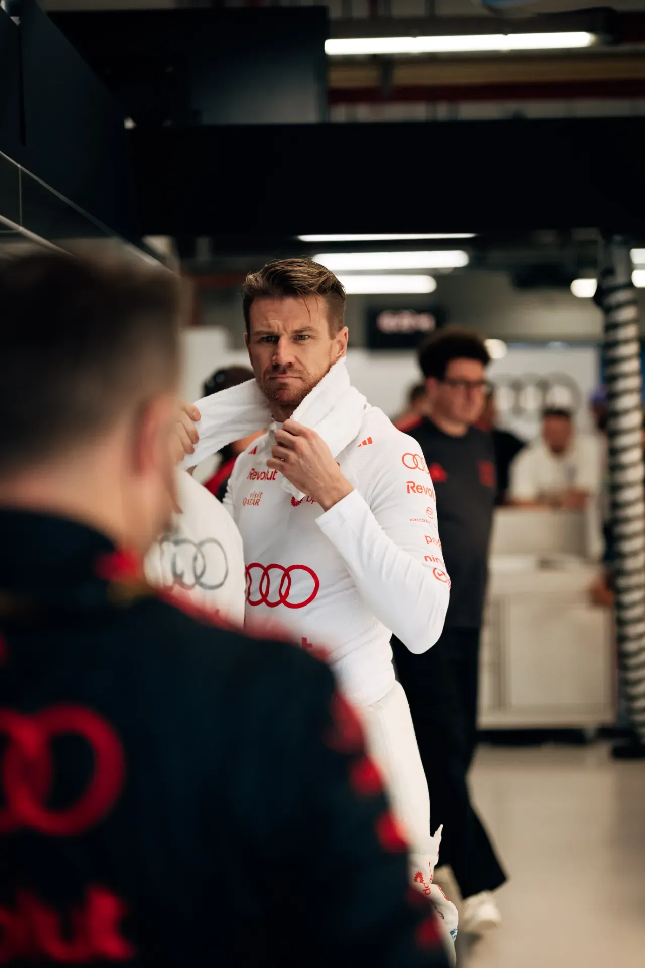 Nico Hulkenberg of the Audi Revolut F1® Team in a white race suit with a towel around his neck in the garage in Singapore