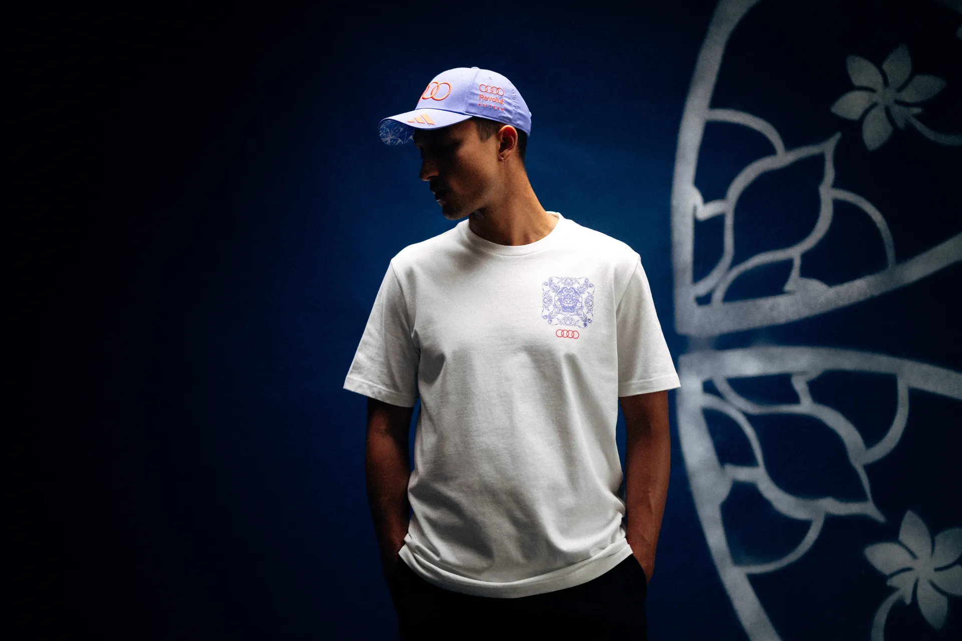 Model wearing an Audi Revolut F1® Team cap and white tee with tile-pattern chest print