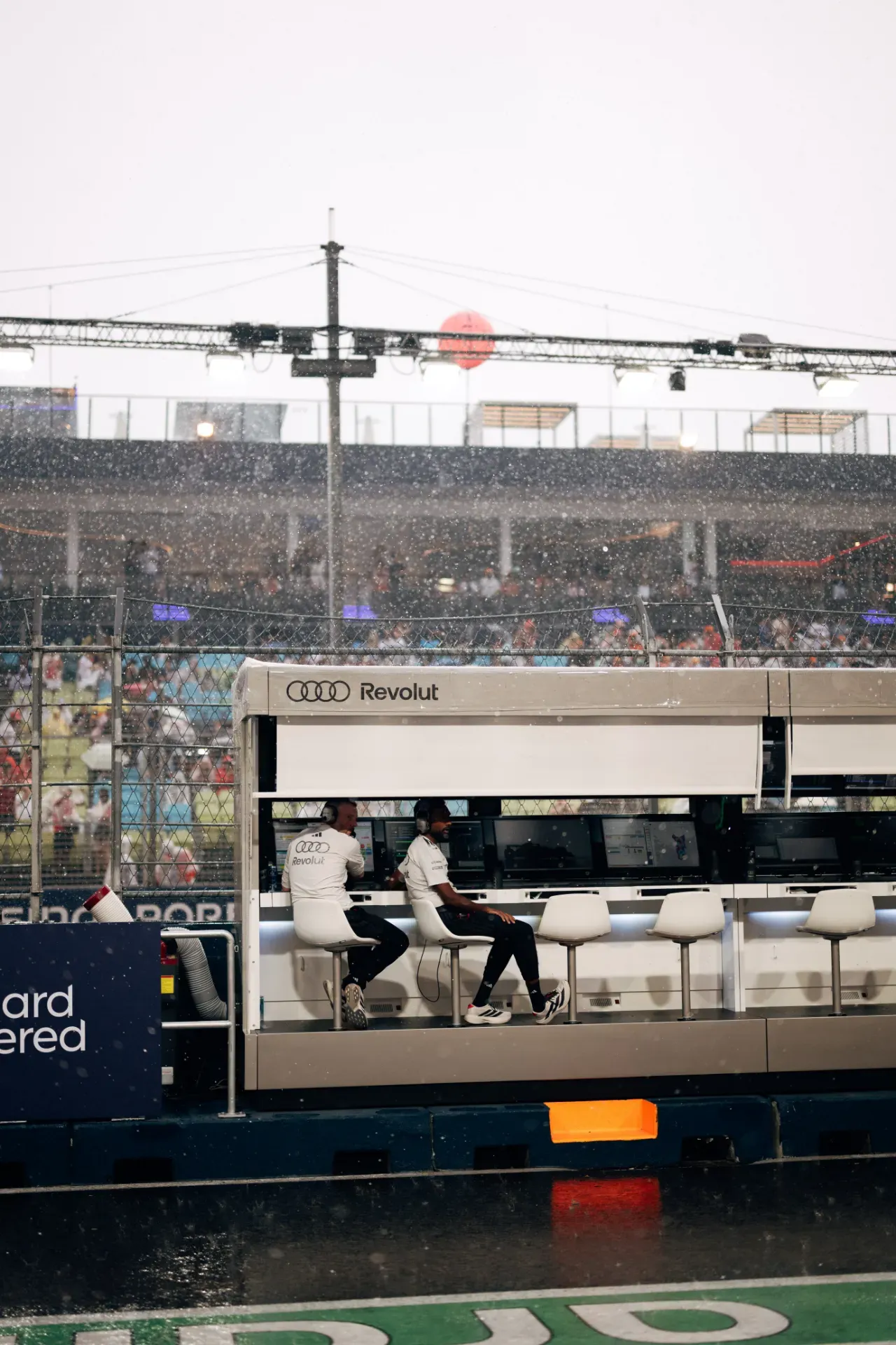 Two team members of the Audi Revolut F1® Team sit with headsets at the pit wall in heavy rain in Singapore