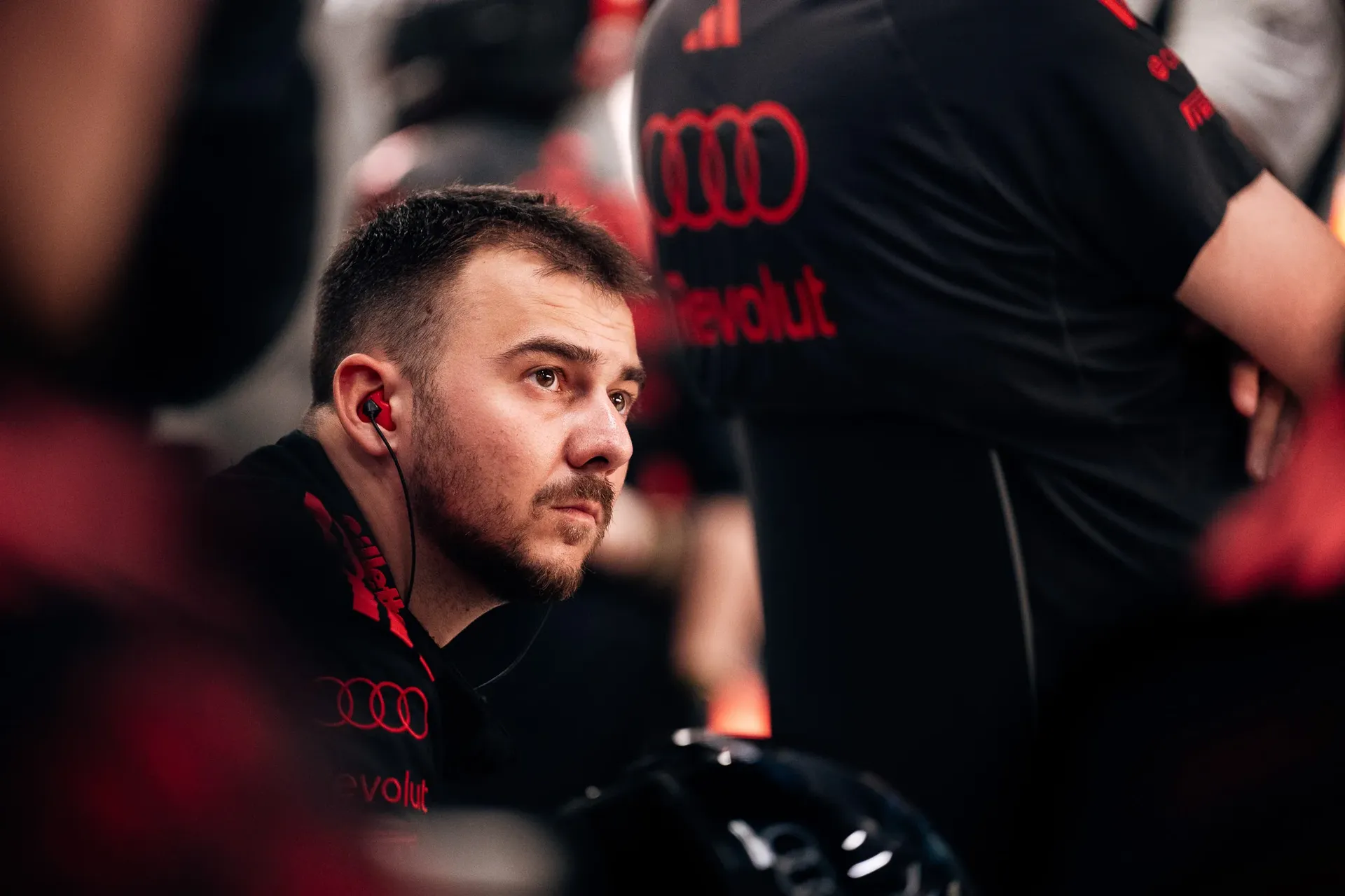 Audi Revolut F1® Team mechanic crouches in the garage, looking ahead, with fellow mechanics blurred in the foreground.