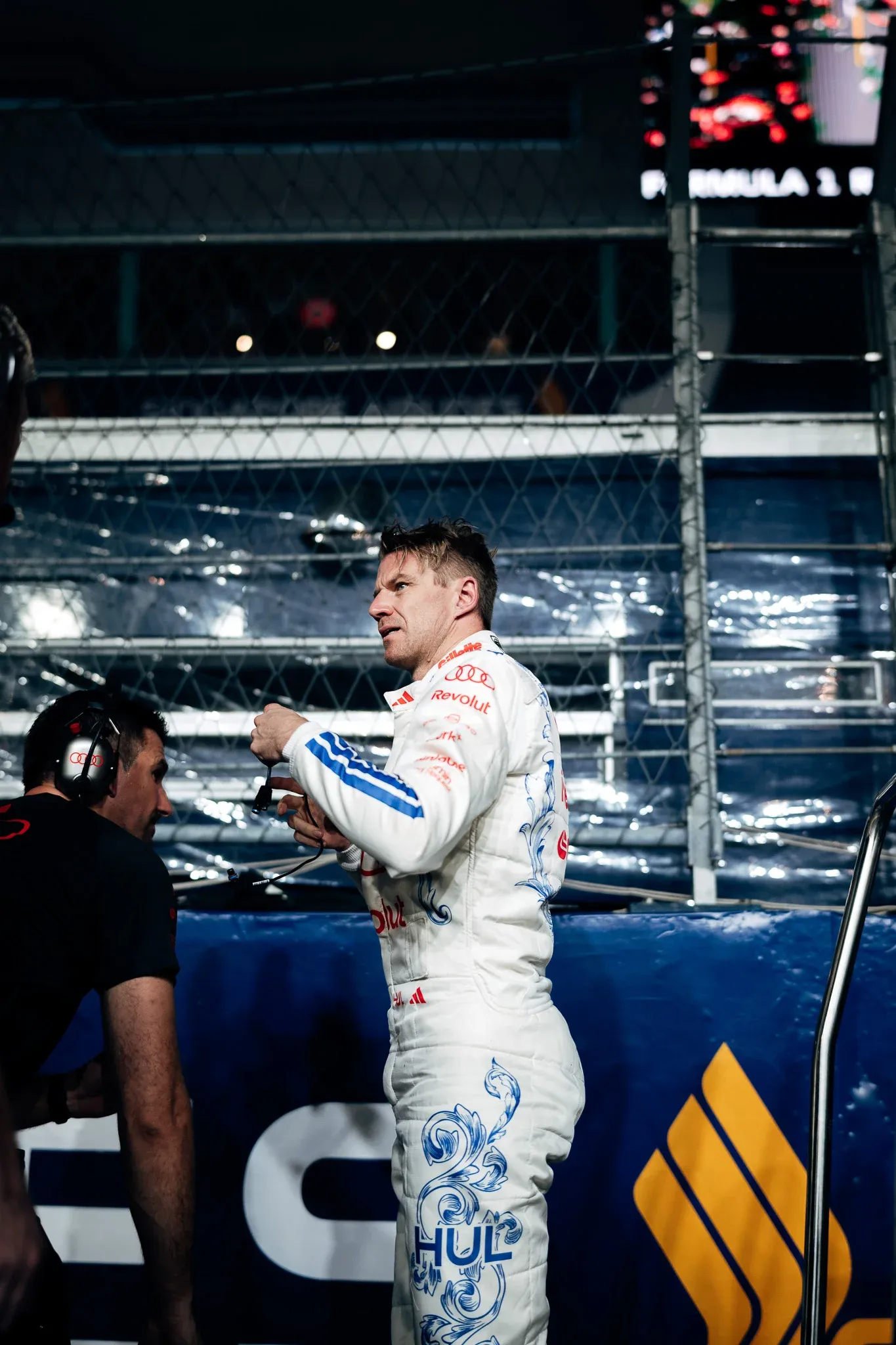 Audi Revolut F1® Team driver Nico Hulkenberg talks with an engineer wearing a headset beside the pit lane barrier.