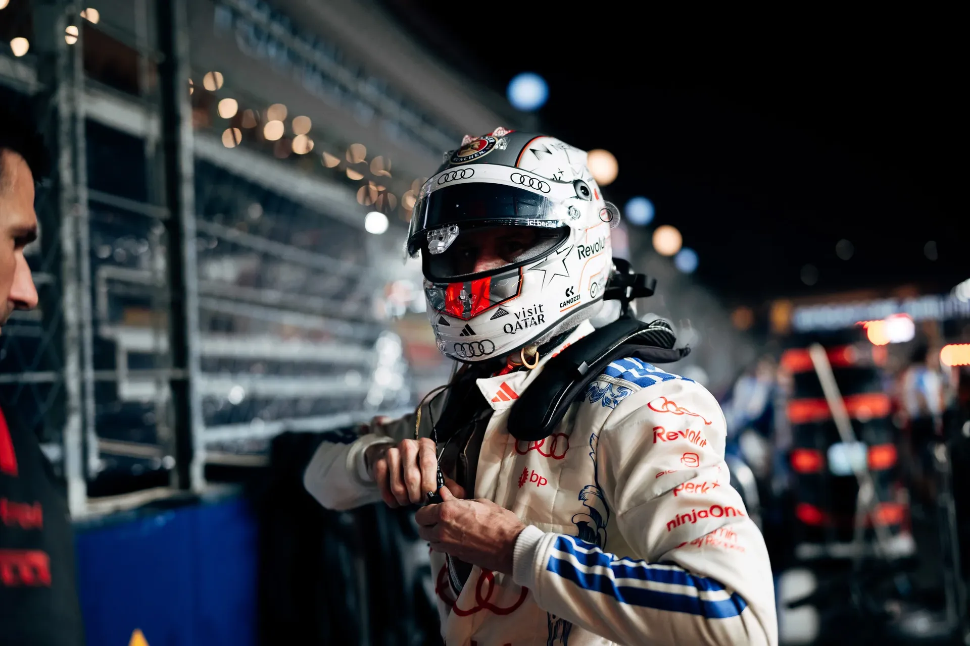 Audi Revolut F1® Team driver Nico Hulkenberg, helmet on and visor up, adjusts his race suit in the illuminated pit lane.